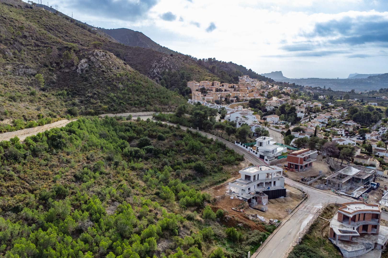 Luftaufnahme des Grundstücks in Monte Olímpico mit befestigten Straßen, im Bau befindlichen Villen und Blick auf die bewaldeten Hänge und das weite Tal.