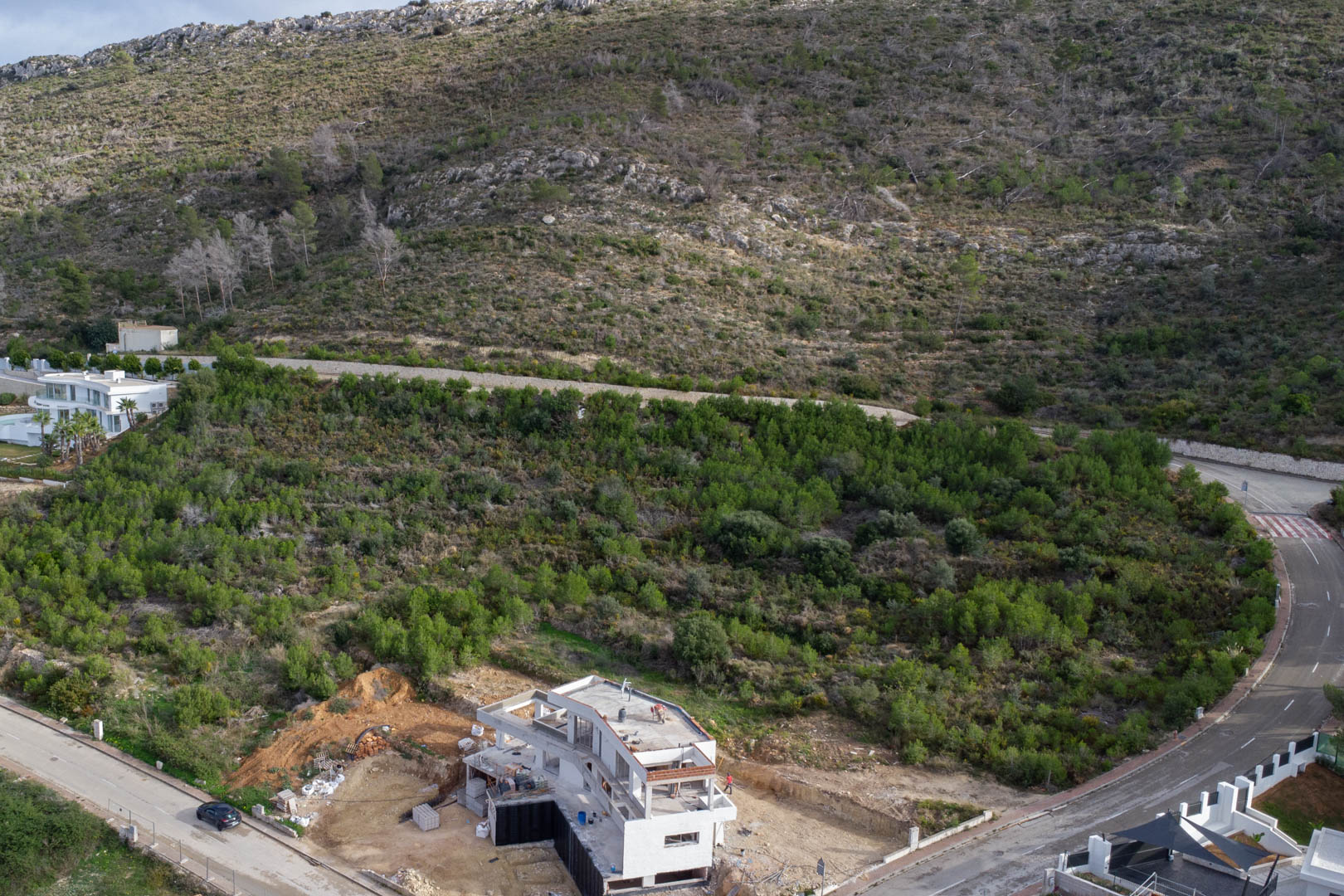 Luftaufnahme des Grundstücks in Monte Olímpico mit fertiggestellter Infrastruktur und einer im Bau befindlichen Villa inmitten mediterraner Vegetation.