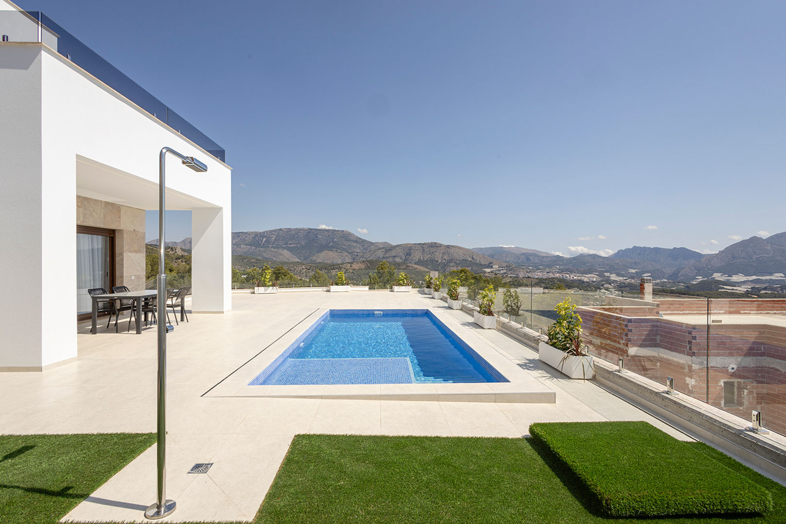 Außen-Terrasse mit privatem Pool, Edelstahldusche und überdachtem Essbereich, mit Glasgeländern und Panoramablick auf die umliegenden Berge.