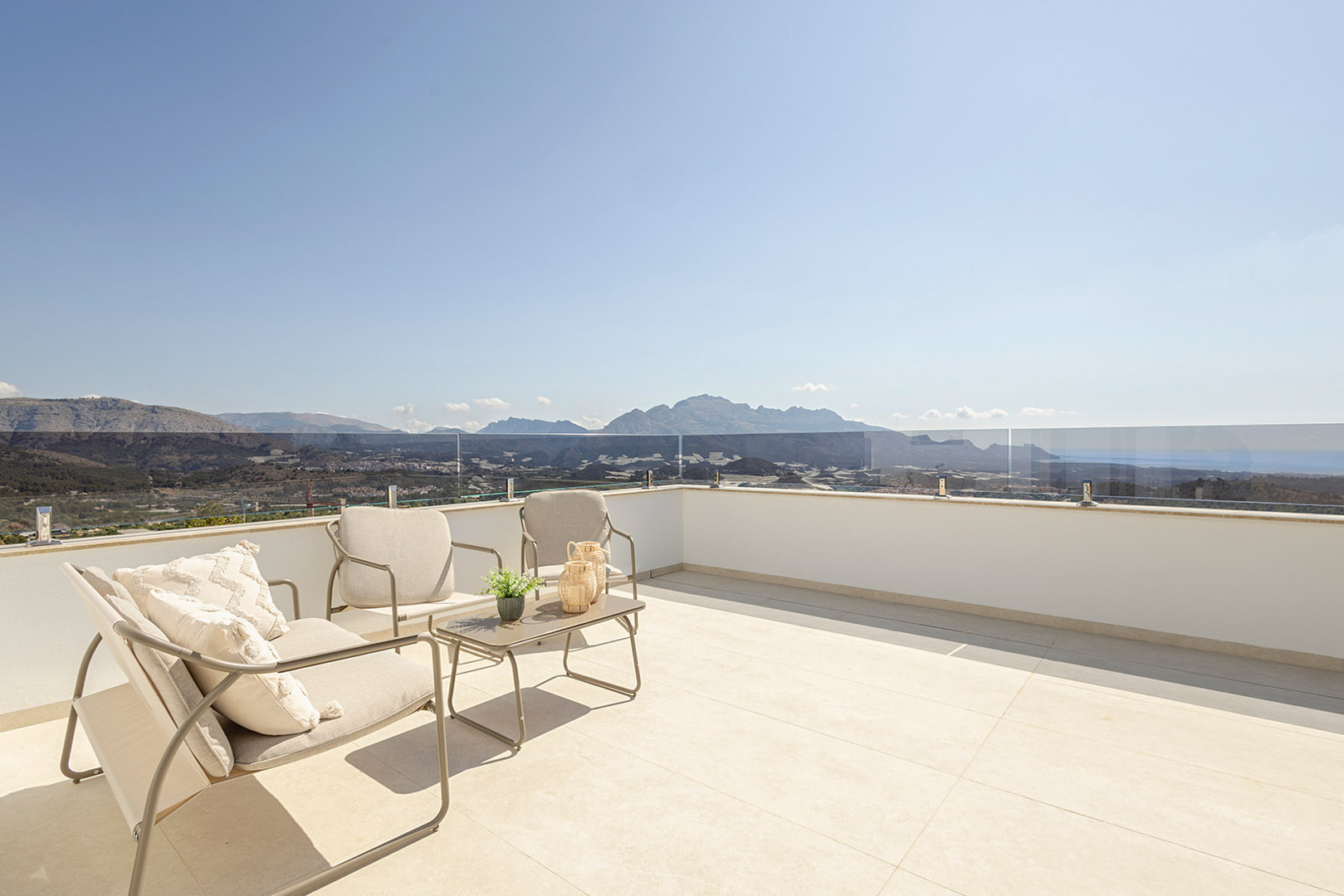 Dakterrasse mit hellen Fliesen, Glasgeländer und modernen Outdoormöbeln mit Panoramablick auf das Meer und die umliegenden Berge.