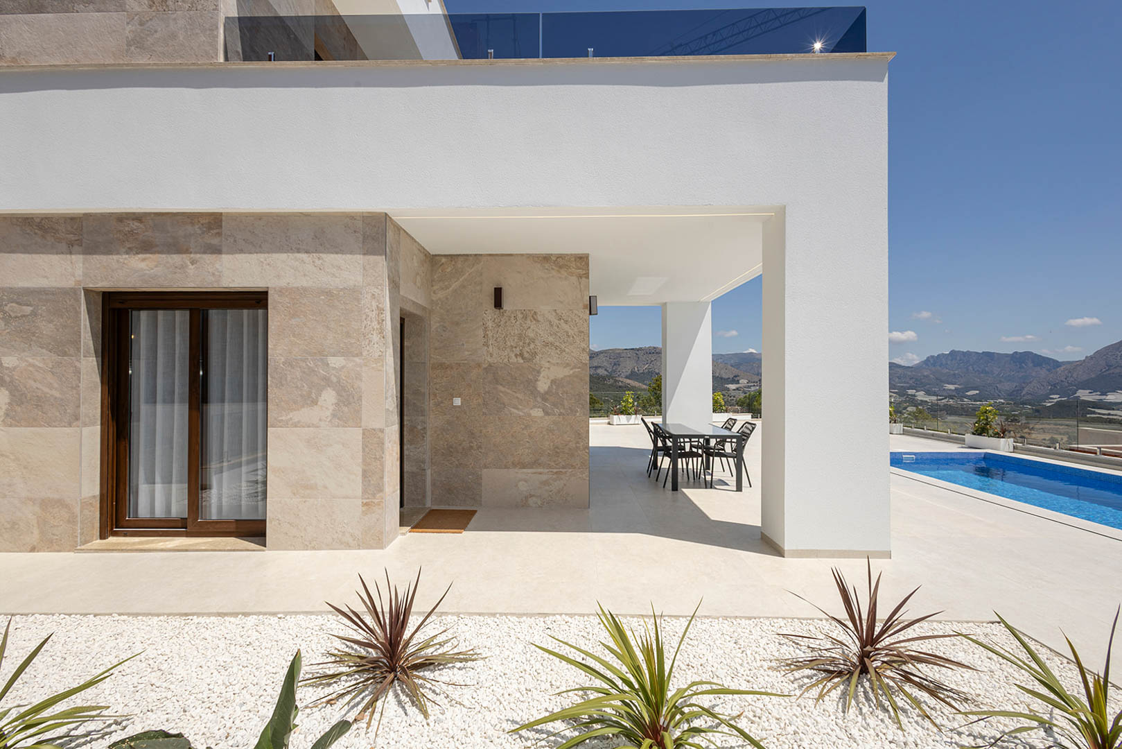 Moderne Villa mit Natursteinverkleidung, überdachter Essterrasse, privatem Pool und weitem Blick auf die umliegende Berglandschaft.