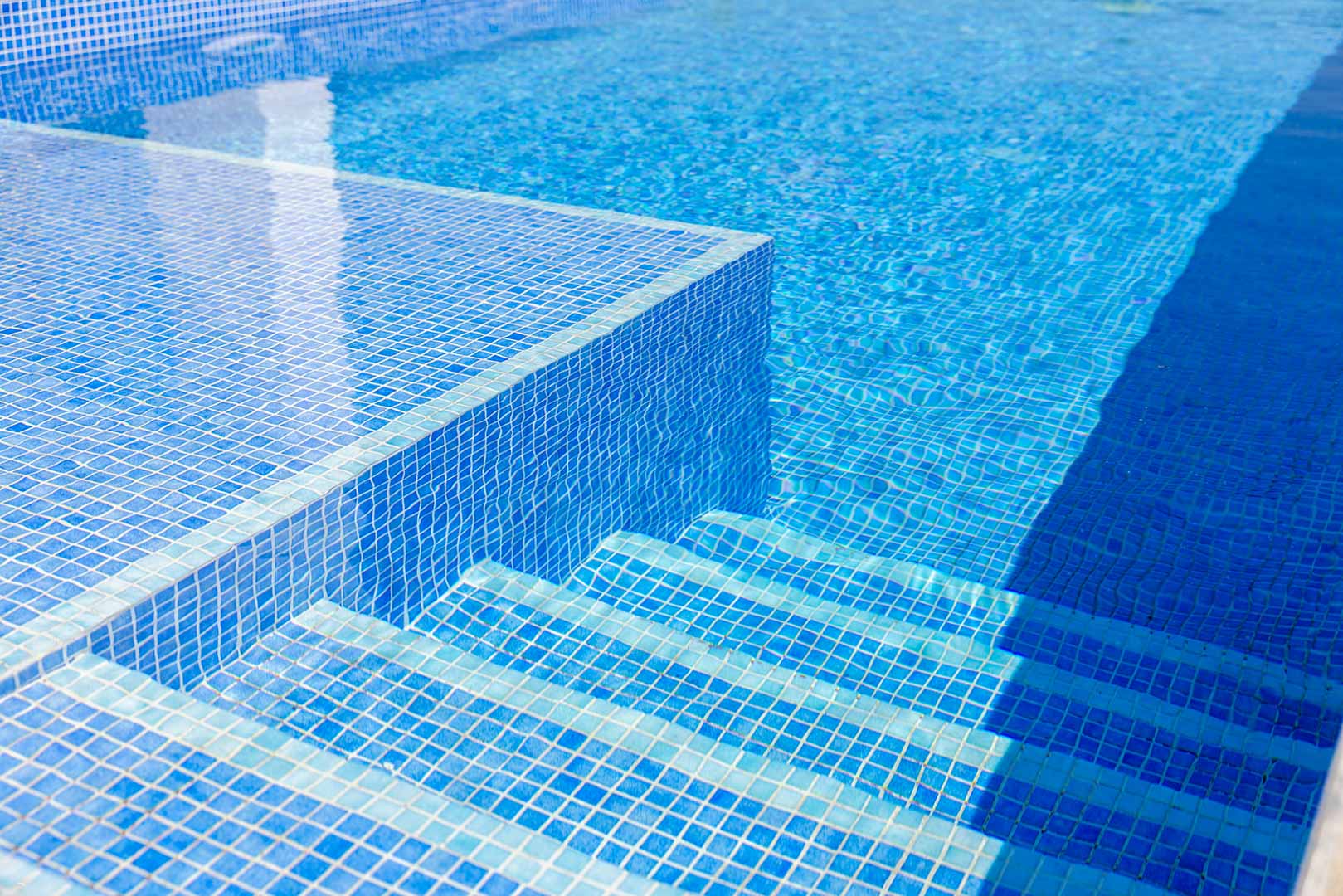 Nahaufnahme des privaten Pools mit blauen Mosaikfliesen und integrierten Unterwassertreppen, die das klare Wasser und moderne Design betonen.