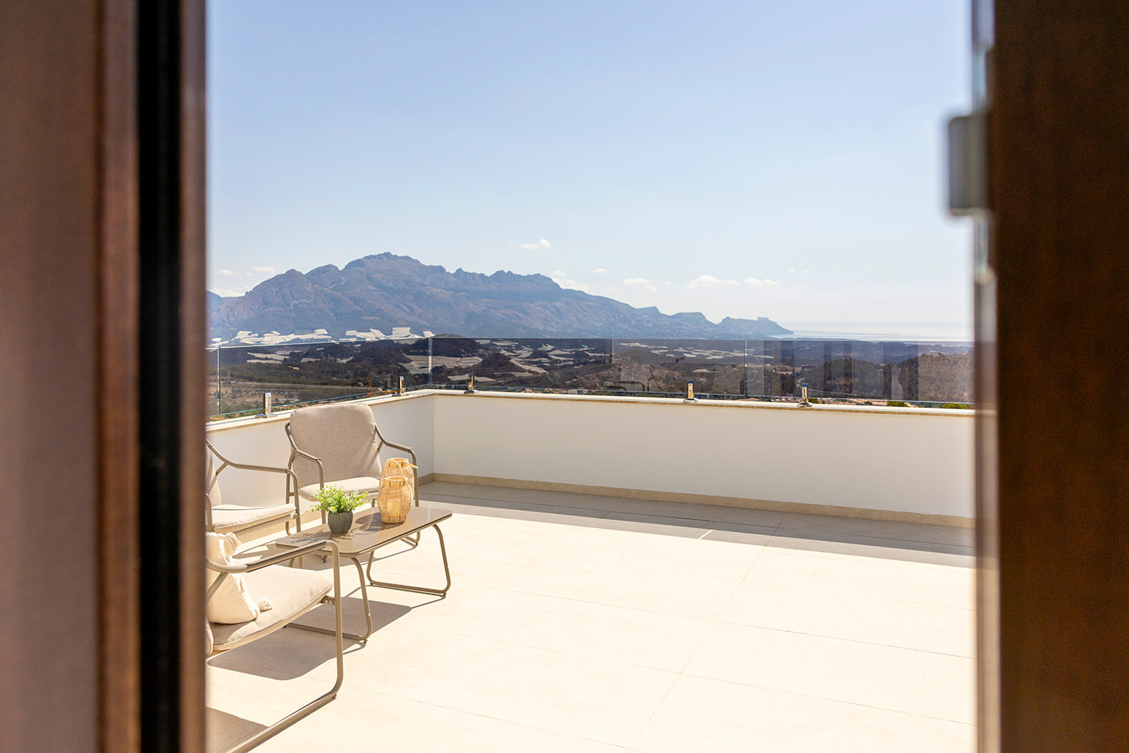 Obere Terrasse mit Glasgeländer, modernen Außenmöbeln und freiem Panoramablick auf die umliegenden Berge und das Mittelmeer.