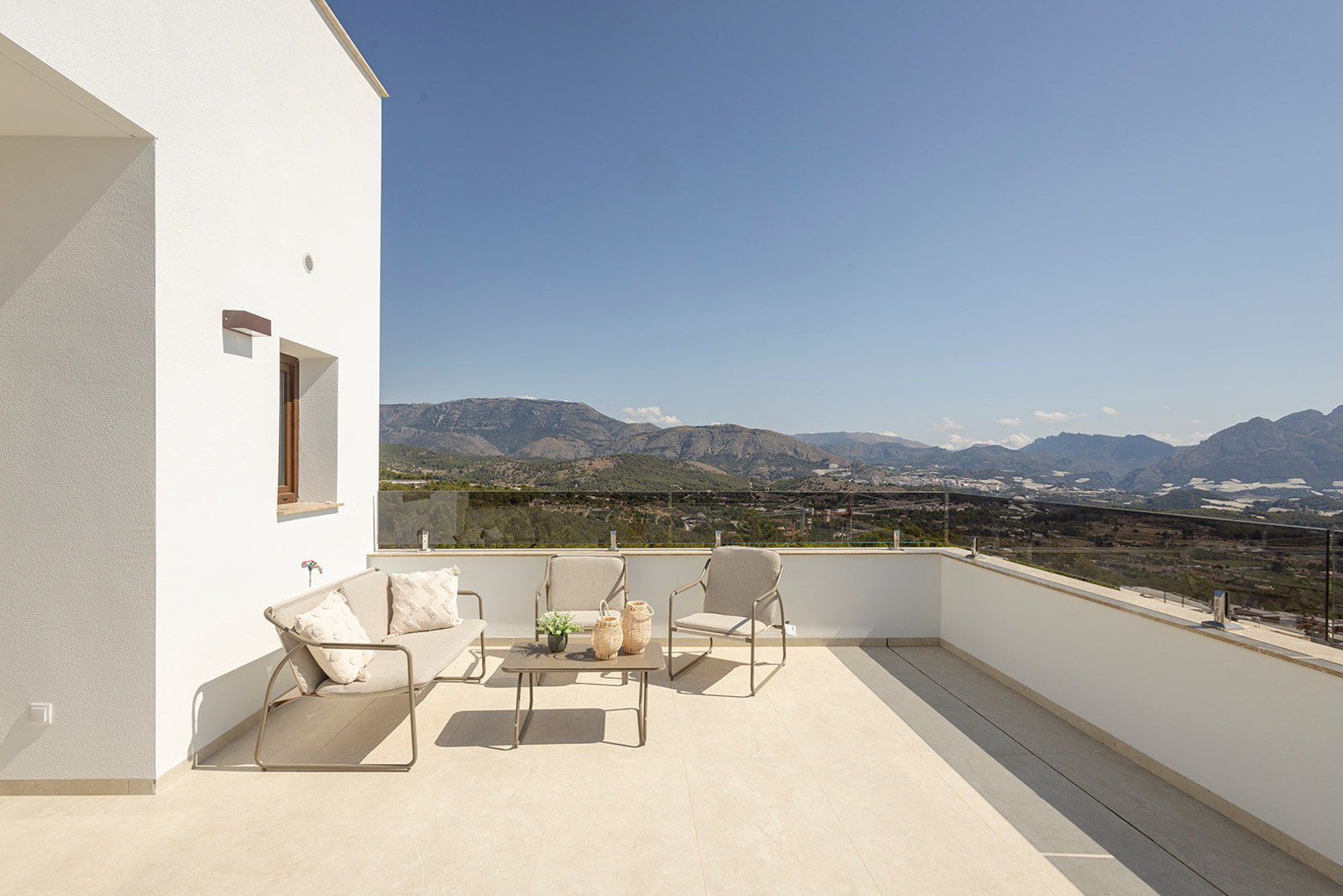 Obere Terrasse mit Glasgeländer und Außenlounge, die einen freien Panoramablick auf die Berge und die umliegende Landschaft bietet.