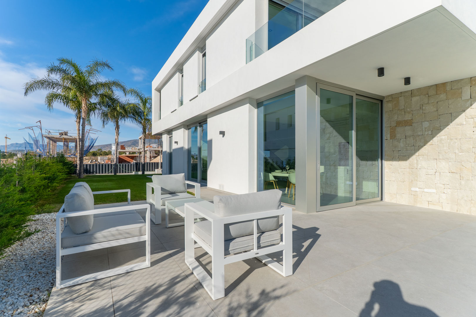Außen-Terrasse mit minimalistischen weißen Möbeln, Feinsteinzeugboden und einer Fassade aus weißem Putz und strukturiertem Naturstein.
