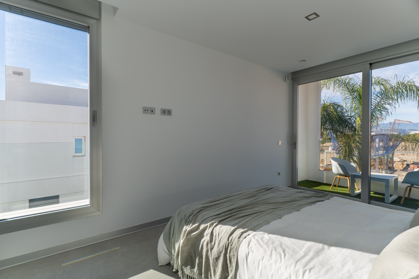 Helles Schlafzimmer mit direktem Zugang zu einem privaten Balkon mit Kunstrasen. Minimalistisches Design, graue Fliesenböden und große Fensterfronten.