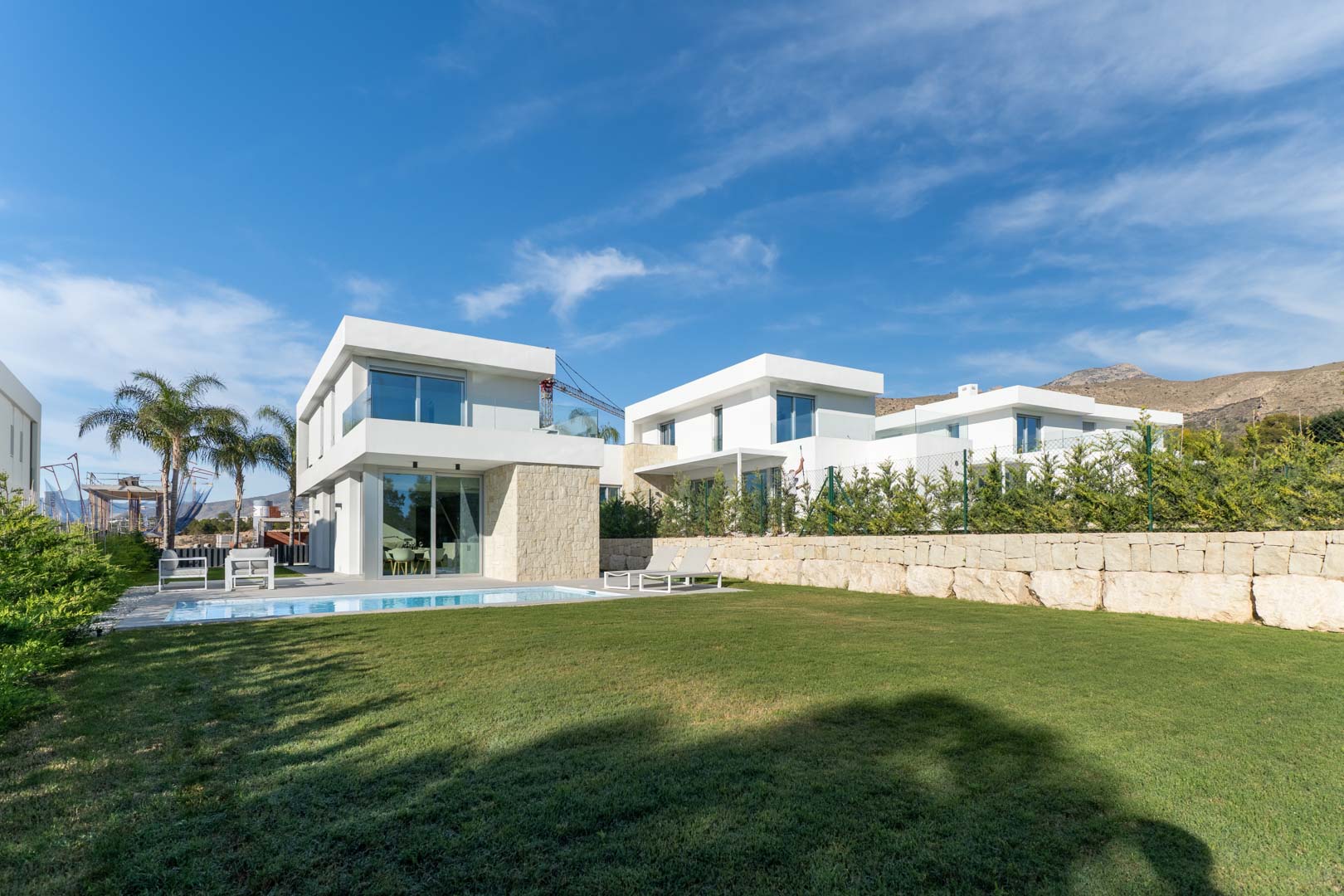 Moderne Villa mit weißer Fassade, Natursteinakzenten, privatem Pool und weitläufigem Rasengarten vor einer markanten Bergkulisse.