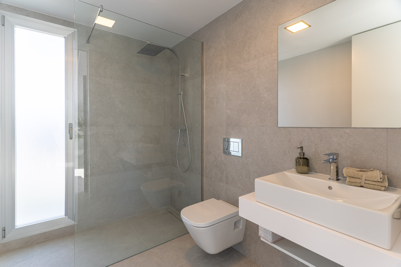 Modernes Badezimmer mit grauen Steinfliesen, begehbarer Glasdusche, wandhängendem WC und einem minimalistischen, schwebenden Waschtisch mit rechteckigem Waschbecken.