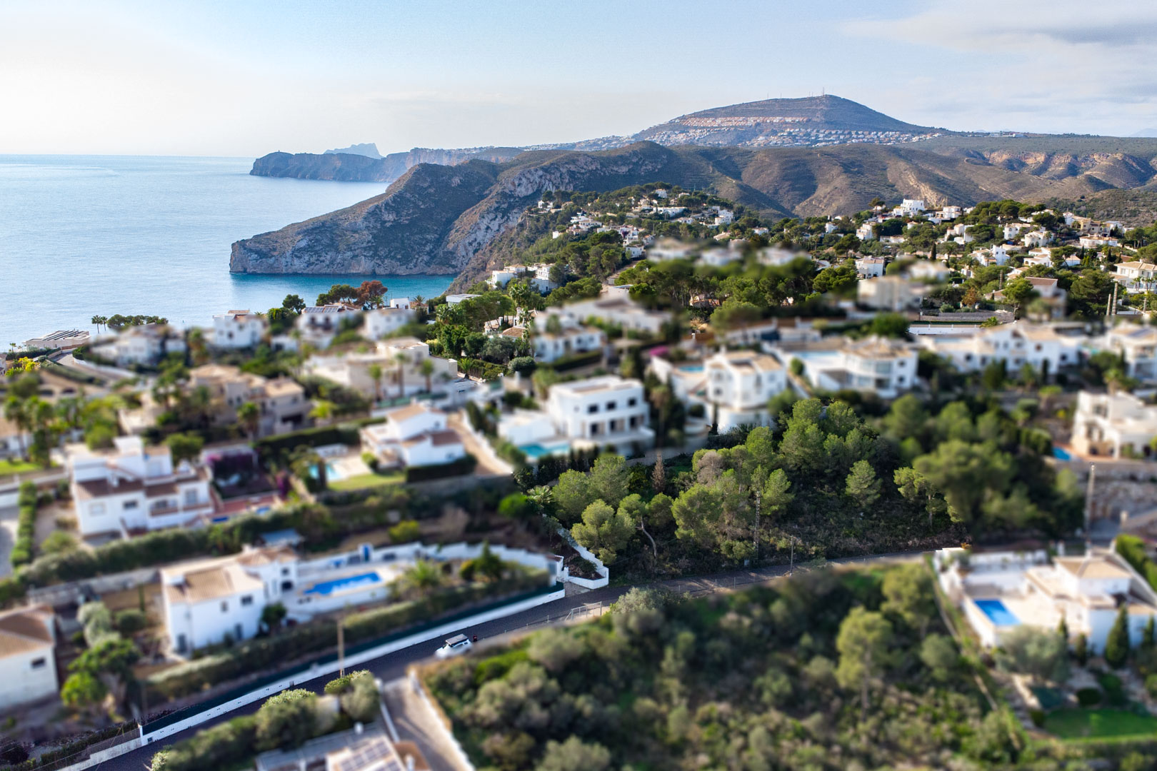 Luftaufnahme im Tilt-Shift-Stil vom Wohngebiet Granadella-Ambolo mit weißen Villen, Pinien und Blick auf die felsige Küste von Jávea.
