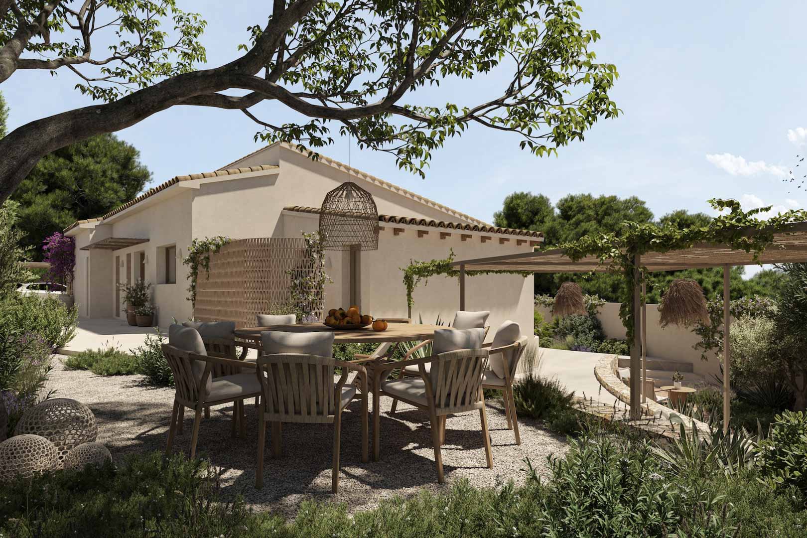 Außenessbereich mit rundem Holztisch und geflochtenen Stühlen auf einer Kiesterrasse, eingebettet in einen mediterranen Garten mit Pergola.