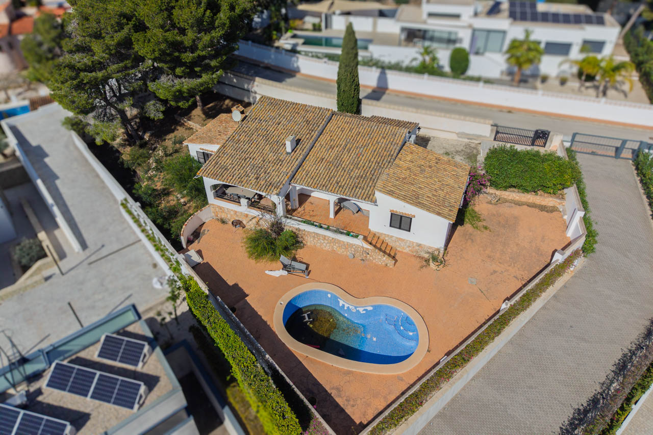 Luftaufnahme der Villa mit ebenem Grundstück, organisch geformtem Pool und mediterraner Architektur mit traditionellen Ziegeldächern und Terrassenflächen.