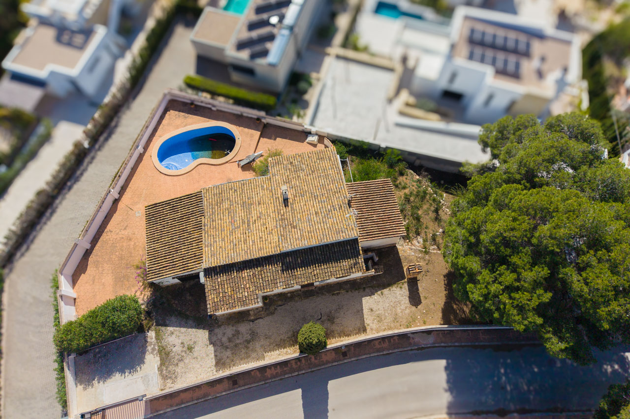 Luftaufnahme der Villa mit ihrem Terrakotta-Ziegeldach, dem organisch geformten Pool und dem flachen Grundstück in einer ruhigen Wohngegend.