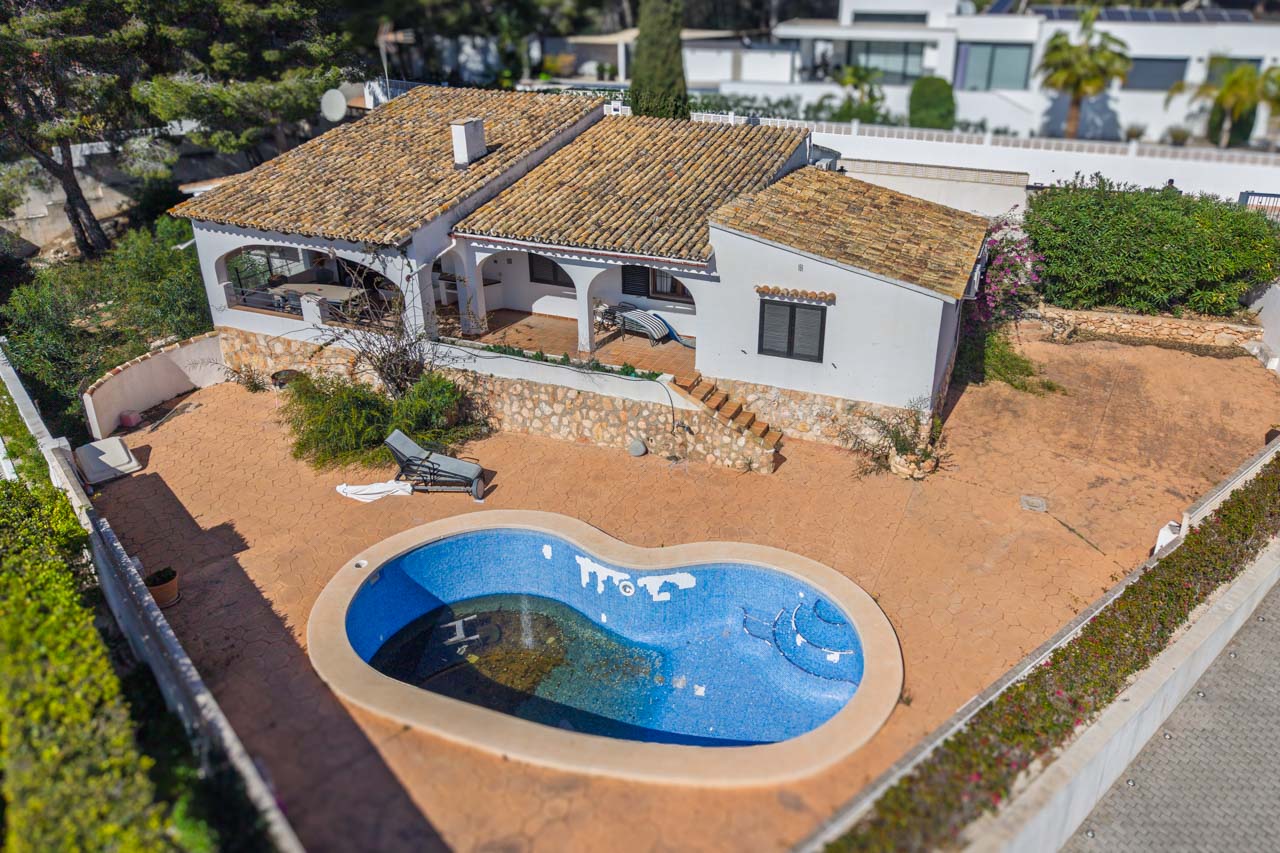 Luftaufnahme der Villa mit organisch geformtem Pool, weitläufigen gepflasterten Terrassen und Rundbogen-Veranden. Die Fassade zeigt Natursteinmauern und ein klassisches Ziegeldach.