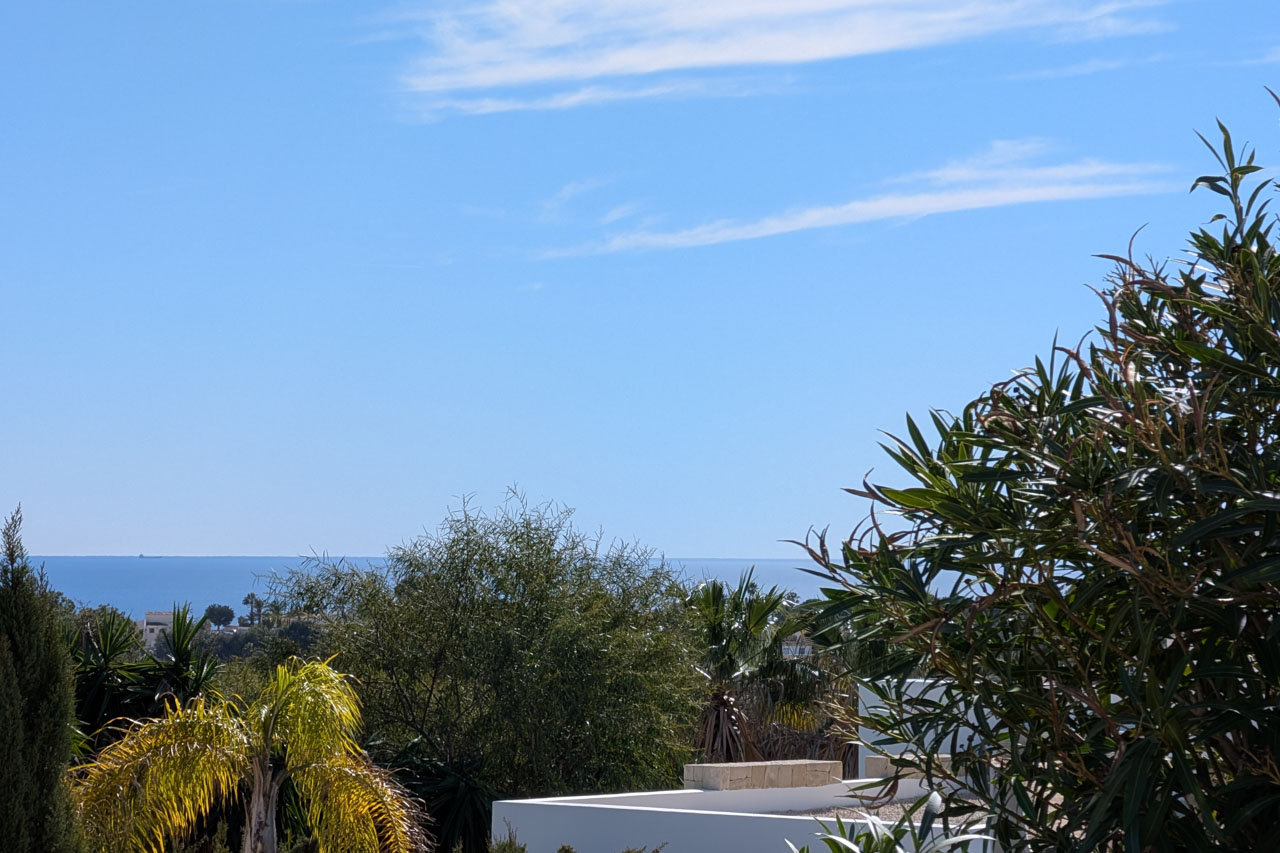 Weitläufiger Blick auf den Horizont des Mittelmeers, eingerahmt von üppiger mediterraner Vegetation und Palmen unter strahlend blauem Himmel.