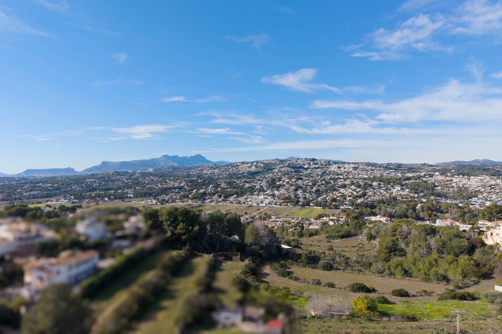 Erhöhter Panoramablick über das Tal von Moraira mit Wohngebieten inmitten der mediterranen Landschaft und markanten Bergsilhouetten im Hintergrund.