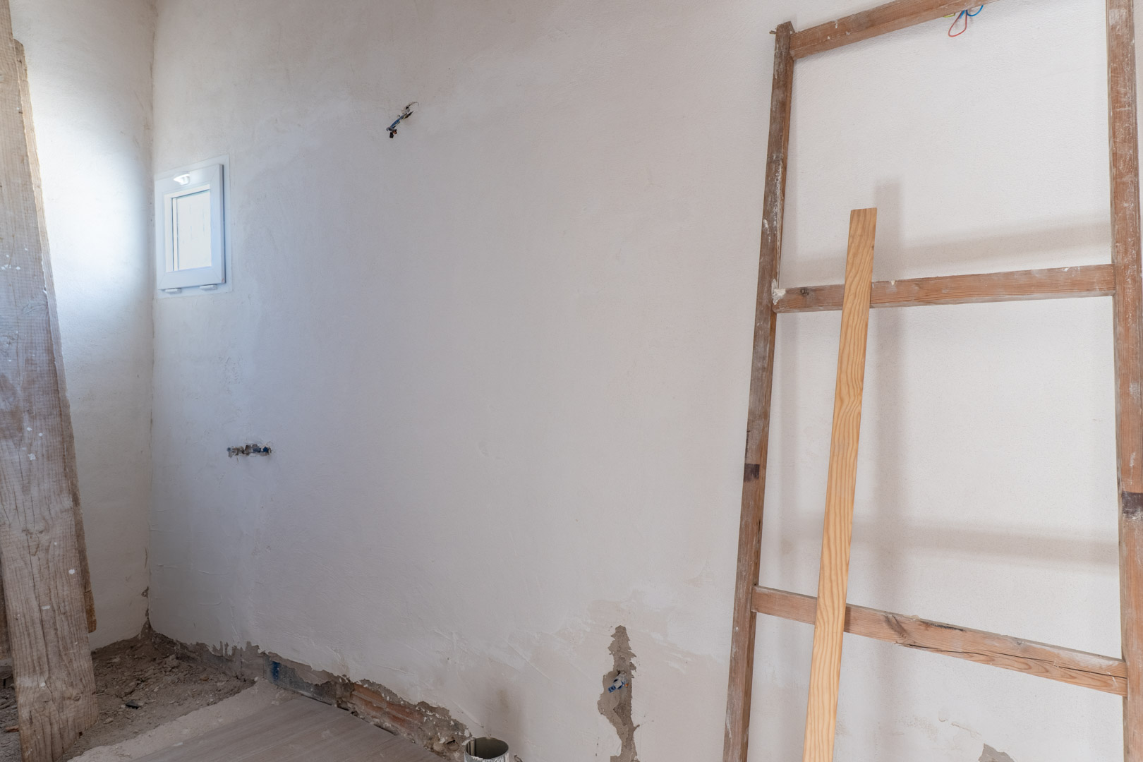Innenraum in der Renovierungsphase mit frisch verputzten Wänden, kleinem weißem Fenster und vorbereiteten Elektroanschlüssen.