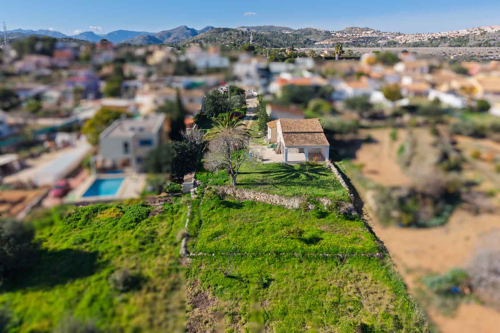 Luftaufnahme der Finca mit renoviertem Ziegeldach und Naya auf einem länglichen Grundstück mit Trockensteinmauern und Blick auf die umliegende Berglandschaft.