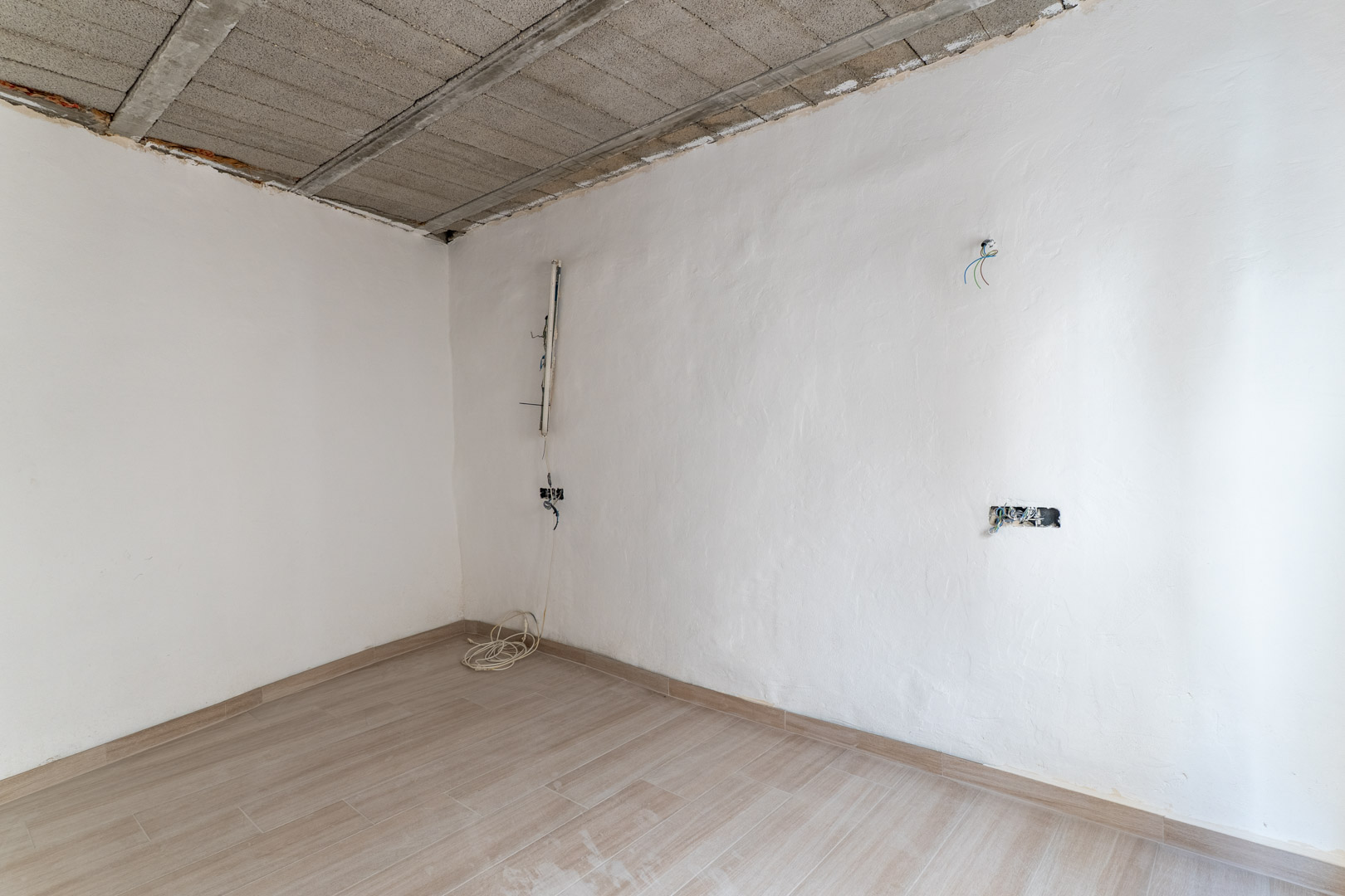 Renovierter Innenraum mit Keramikboden in Holzoptik, weißen Wänden und einer Decke aus Betonbalken mit sichtbarer Elektrovorinstallation.