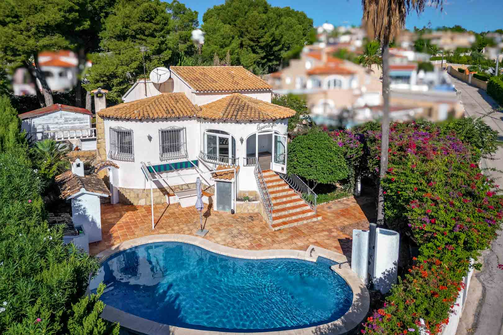 Außenansicht der Villa mit nierenförmigem Pool, Terrakotta-Terrasse und Treppenaufgang zur verglasten Veranda, eingebettet in einen mediterranen Garten.