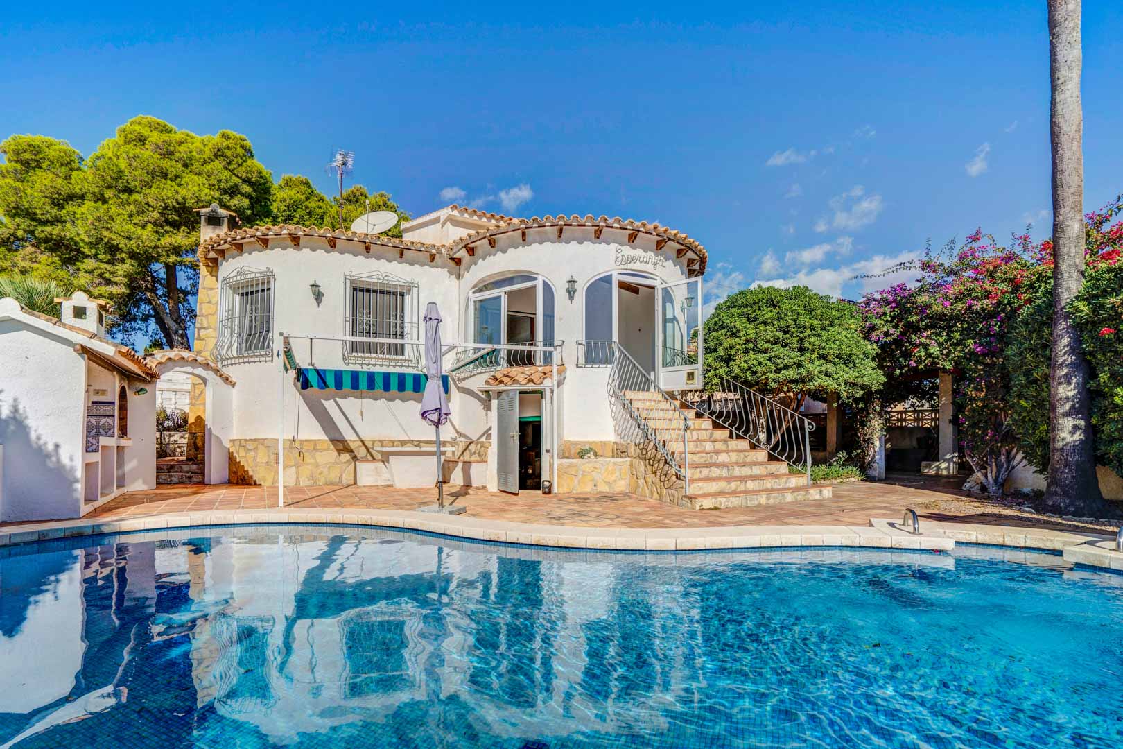 Außenansicht der Villa mit privatem Pool, weißer Rundfassade und Steintreppe, die zur verglasten Terrasse führt, umgeben von mediterraner Vegetation.