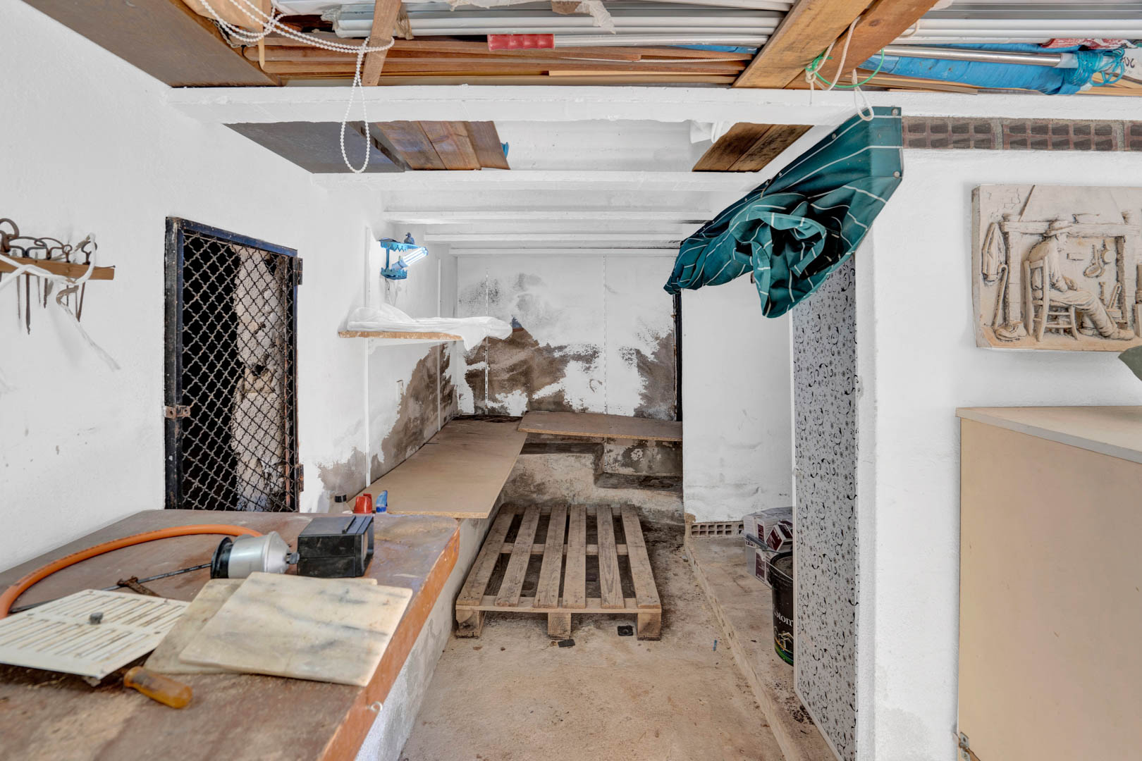 Funktionaler Halbkeller, der als Lager- und Werkstattraum genutzt wird, mit sichtbaren Deckenbalken, Werkbänken aus Holz und vielseitigem Stauraum.