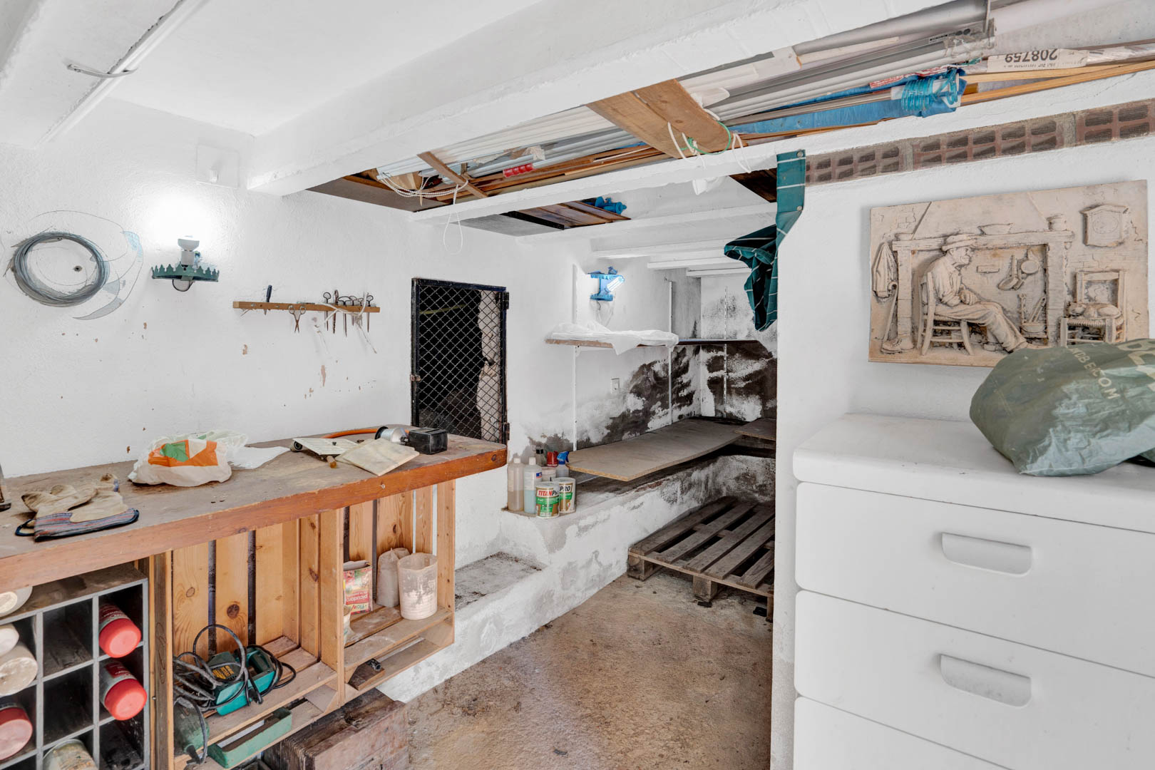 Funktionaler Souterrain-Lagerraum mit Werkbank aus Holz, weiß getünchten Wänden und vielseitigen Abstellmöglichkeiten für Werkzeuge und Instandhaltung.