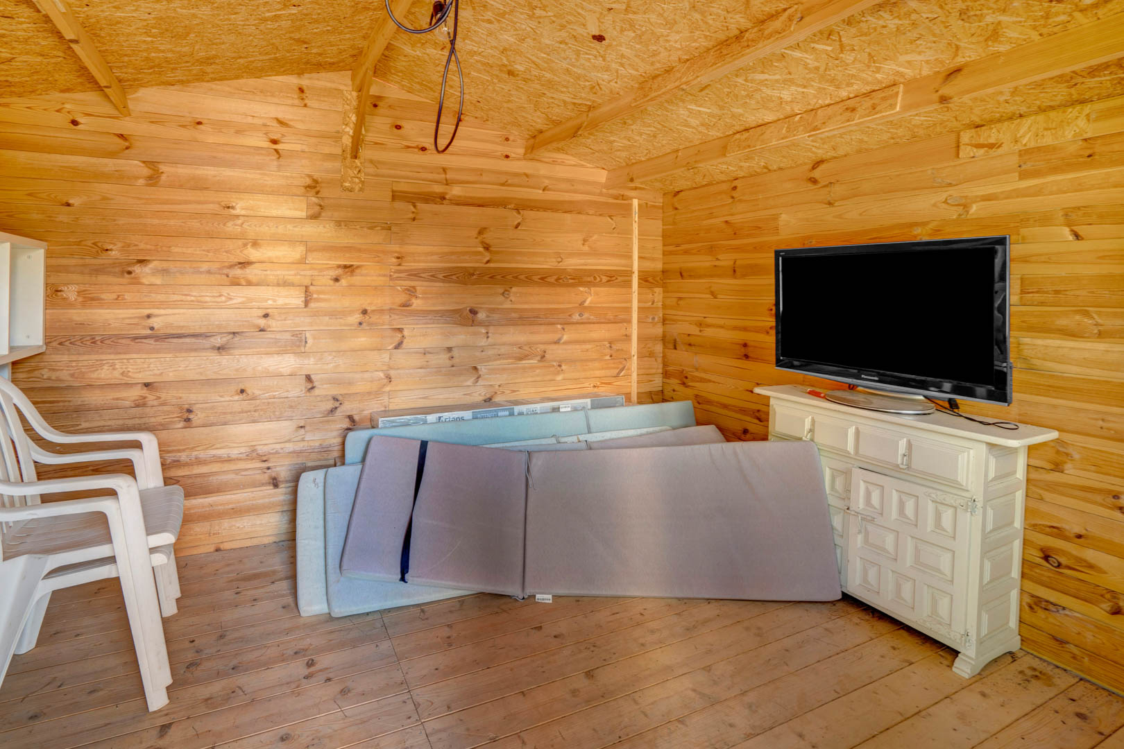 Gartenhaus aus Holz mit Kiefernholzwänden, ausgestattet mit einem Sideboard, Fernseher und Stauraum für Gartenmöbel-Auflagen.