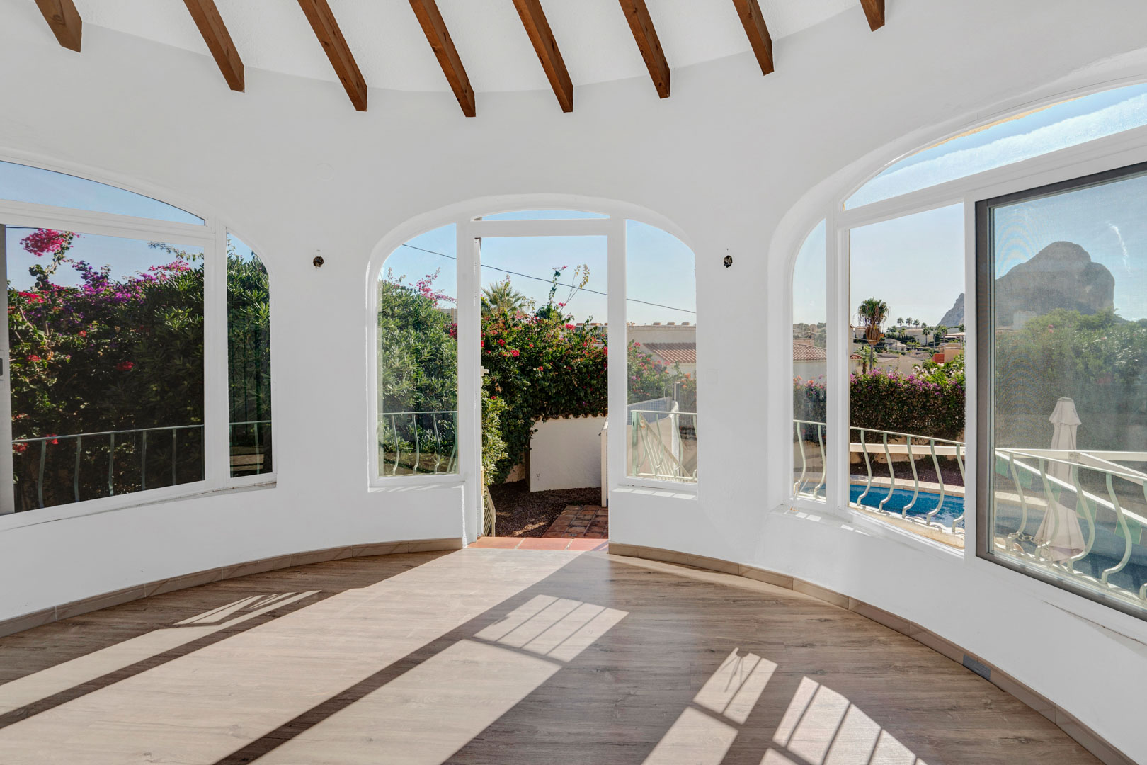 Verglaste Terrasse mit sichtbaren Holzbalken, Laminatboden und Rundbogenfenstern mit Blick auf den Peñón de Ifach und den privaten Poolbereich.