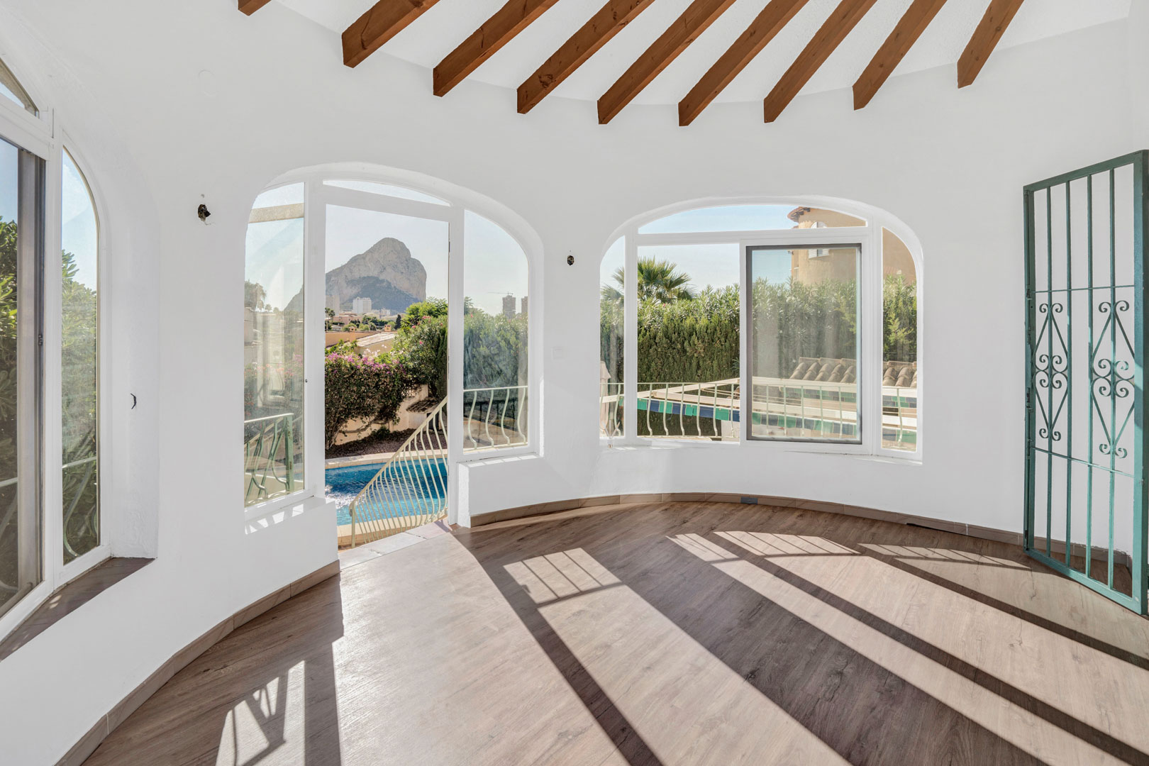 Verglaste Terrasse mit sichtbaren Holzbalken, Laminatboden und Rundbogenfenstern mit direktem Blick auf den Peñón de Ifach und den privaten Pool.