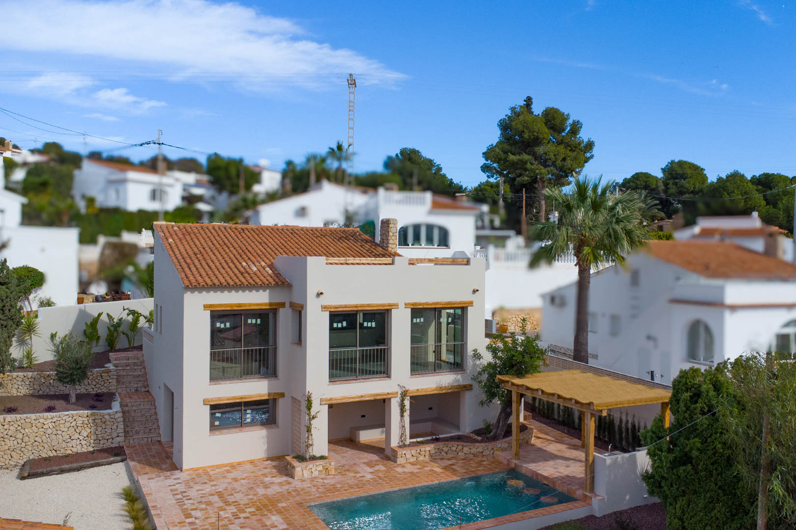 Außenansicht der mediterranen Villa mit großen Fensterfronten, Terrakottadach, privatem Poolbereich, Holzpergola und Natursteinmauern im Garten.