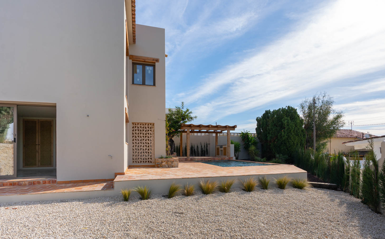 Außenansicht der Villa mit Terrakotta-Terrasse, neu gebautem Pool und Holzpergola über dem Grillbereich, eingebettet in einen pflegeleichten Kiesgarten.