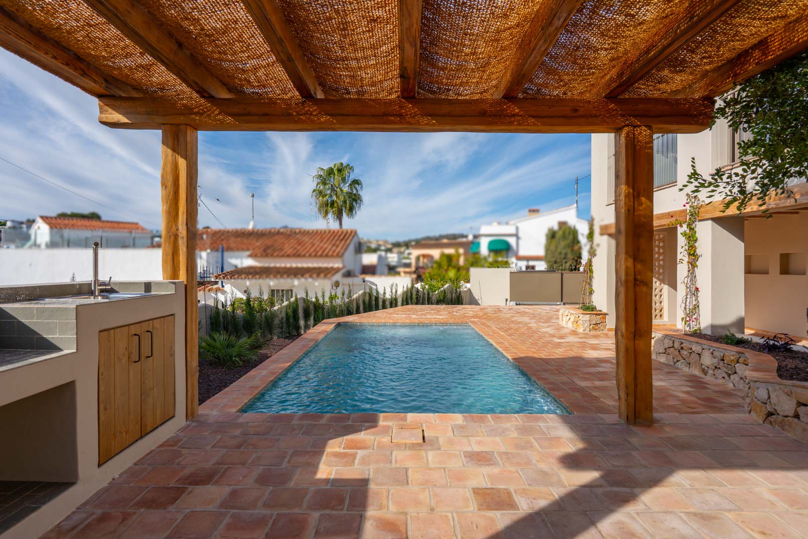 Außenbereich mit Terrakotta-Fliesen, einer Holzpergola und Grillstation direkt am neu angelegten Pool in mediterraner Umgebung.