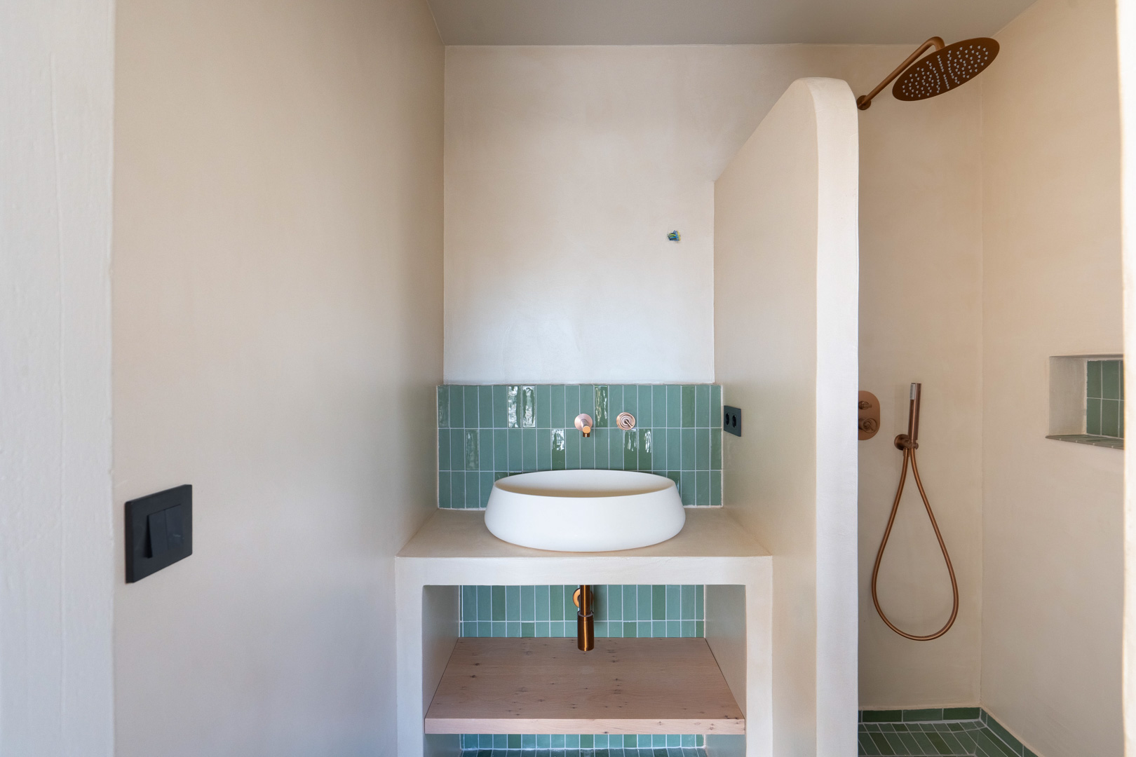 Badezimmer mit Aufsatzwaschbecken, Kupferarmaturen und grünen vertikalen Fliesen. Lehmputzwände und begehbare Dusche mit geschwungener Trennwand.