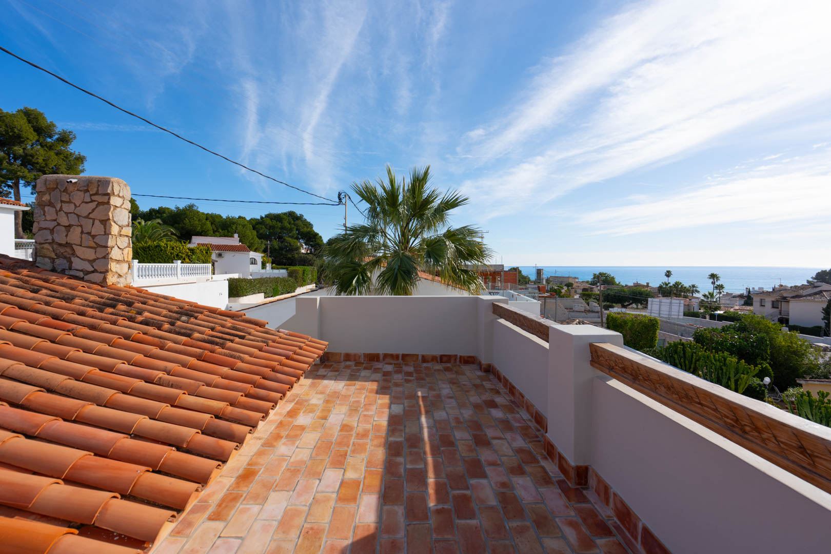 Dachterrasse mit Terrakotta-Fliesen und Panoramablick auf das Mittelmeer. Zu sehen sind ein Natursteinkamin und traditionelle Dachziegel in einer ruhigen Küstenlage.