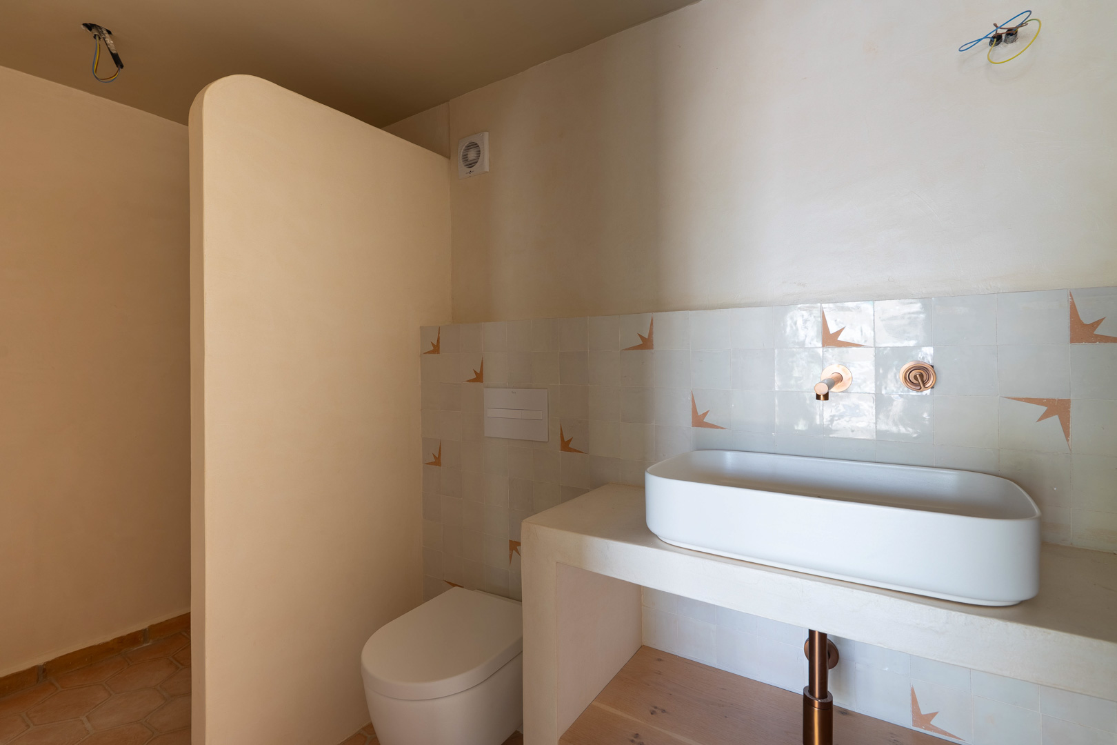 Design-Badezimmer mit Aufsatzwaschbecken auf gemauertem Waschtisch, Unterputz-Kupferarmaturen und Lehmputzwänden. Mit wandhängendem WC und Terrakottaboden.