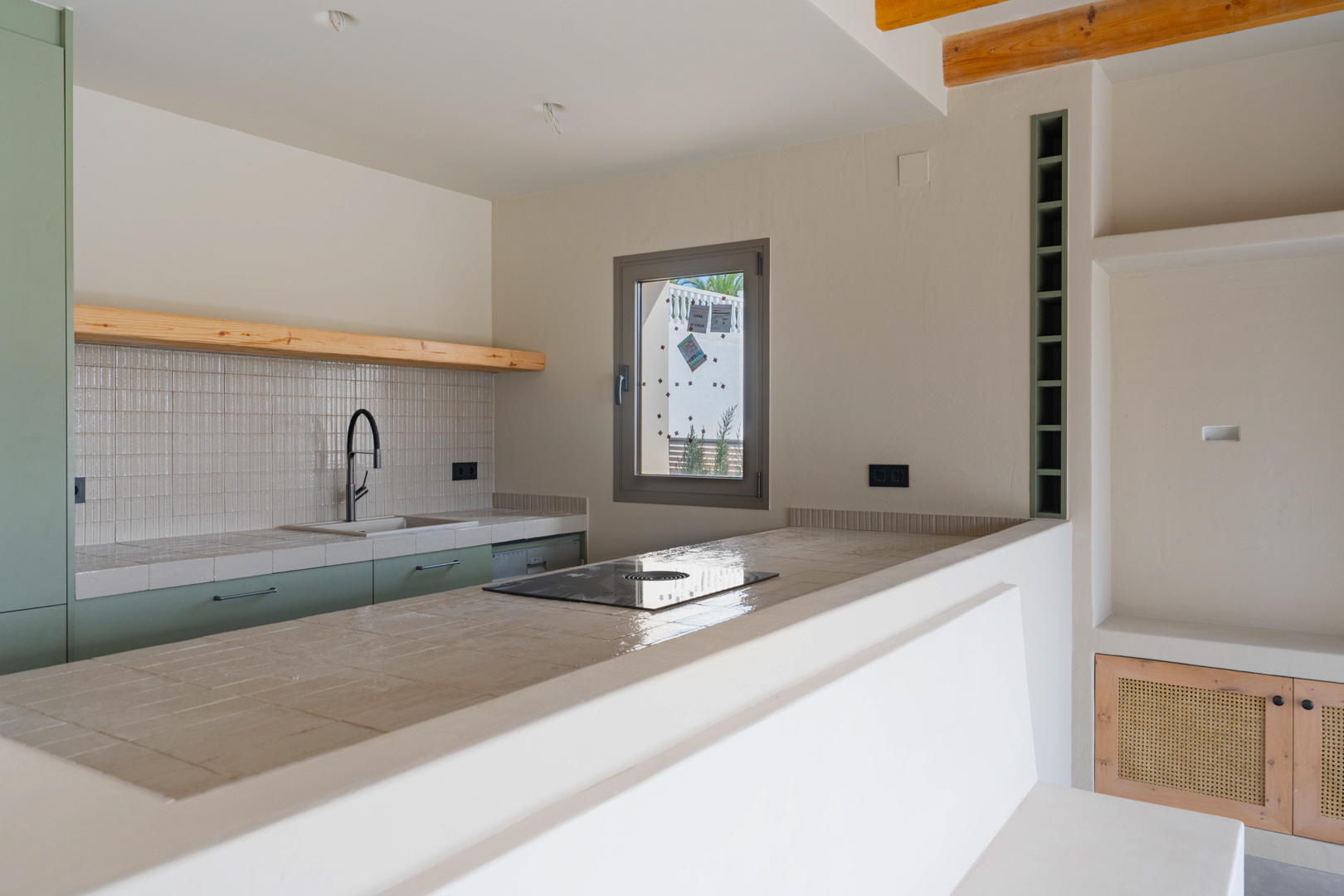 Designerküche mit Porzellan-Arbeitsplatten, integriertem Induktionskochfeld und salbeigrünen Schränken. Lehmputzwände und Akzente aus Naturholz sorgen für ein warmes Ambiente.