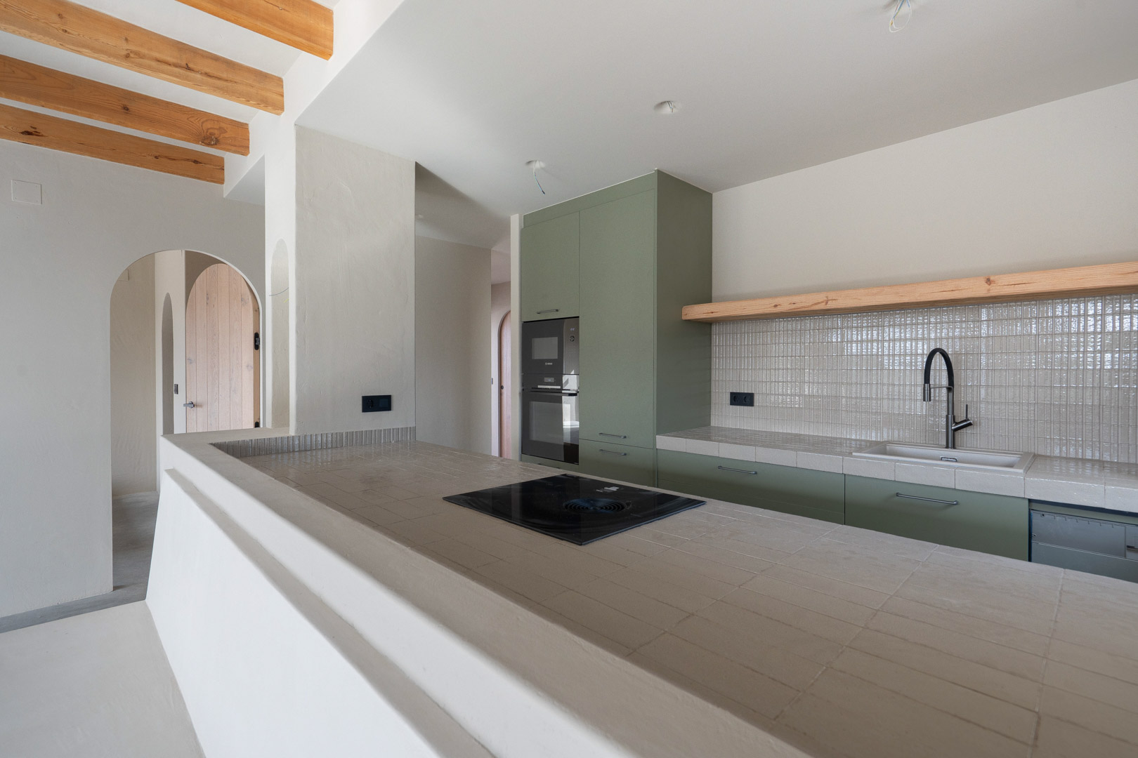 Designerküche mit salbeigrünen Fronten, Ragno-Porzellan-Arbeitsplatten und Bora-Kochfeld. Sichtbare Holzbalkendecke und Wände mit natürlichem Lehmputz.