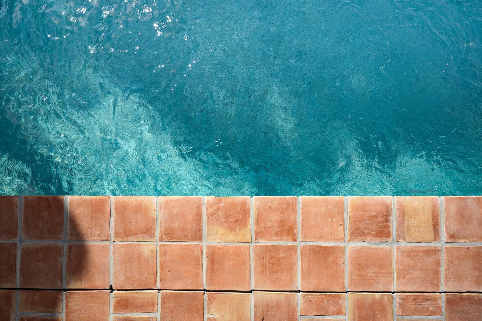 Draufsicht auf den Poolrand mit natürlichen Terrakotta-Fliesen und kristallklarem, türkisfarbenem Wasser im charakteristischen mediterranen Design.