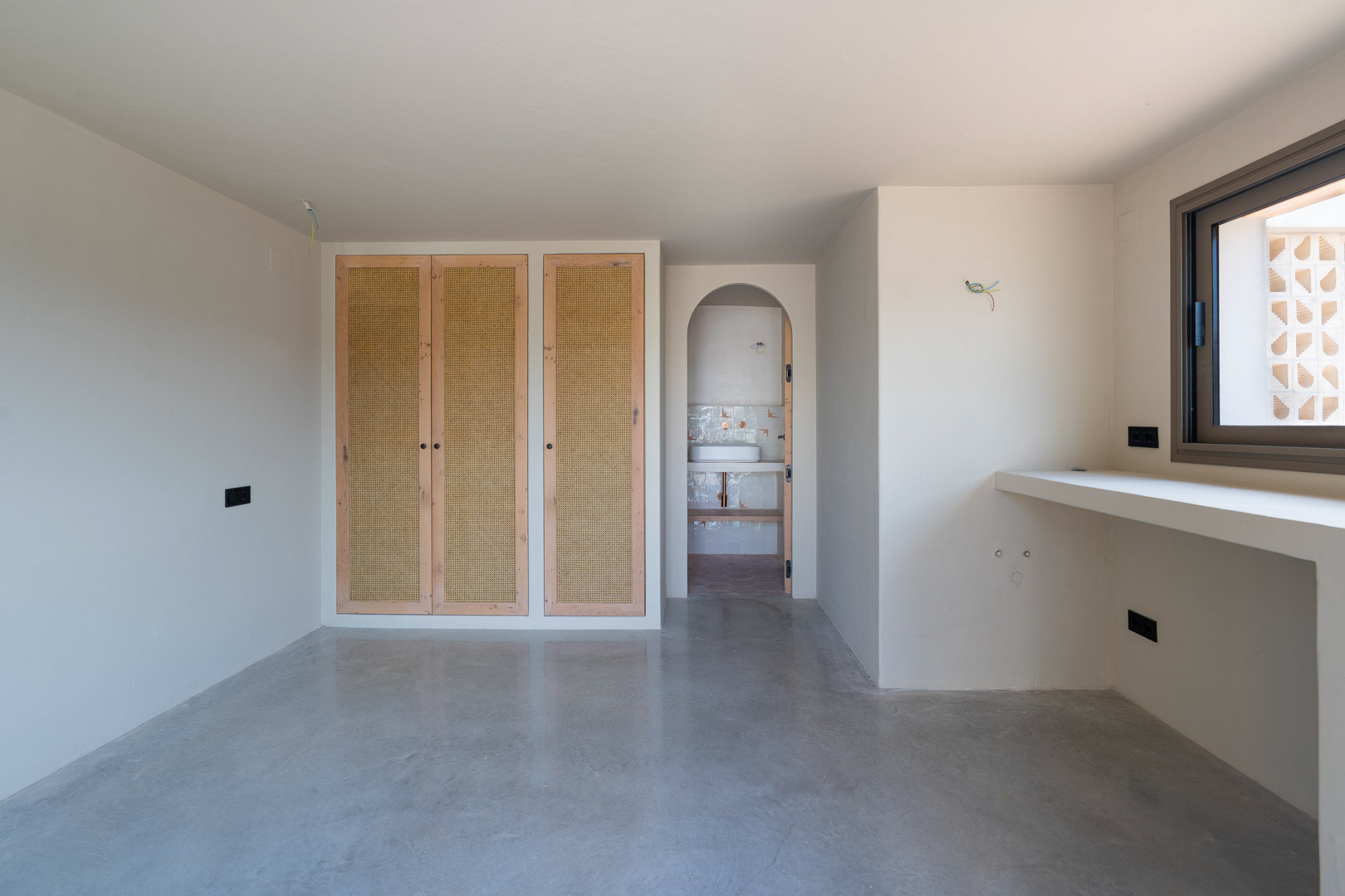 Schlafzimmer mit Einbauschränken aus Eichenholz und Wiener Geflecht, poliertem Betonboden und Rundbogen-Zugang zum En-Suite-Badezimmer.