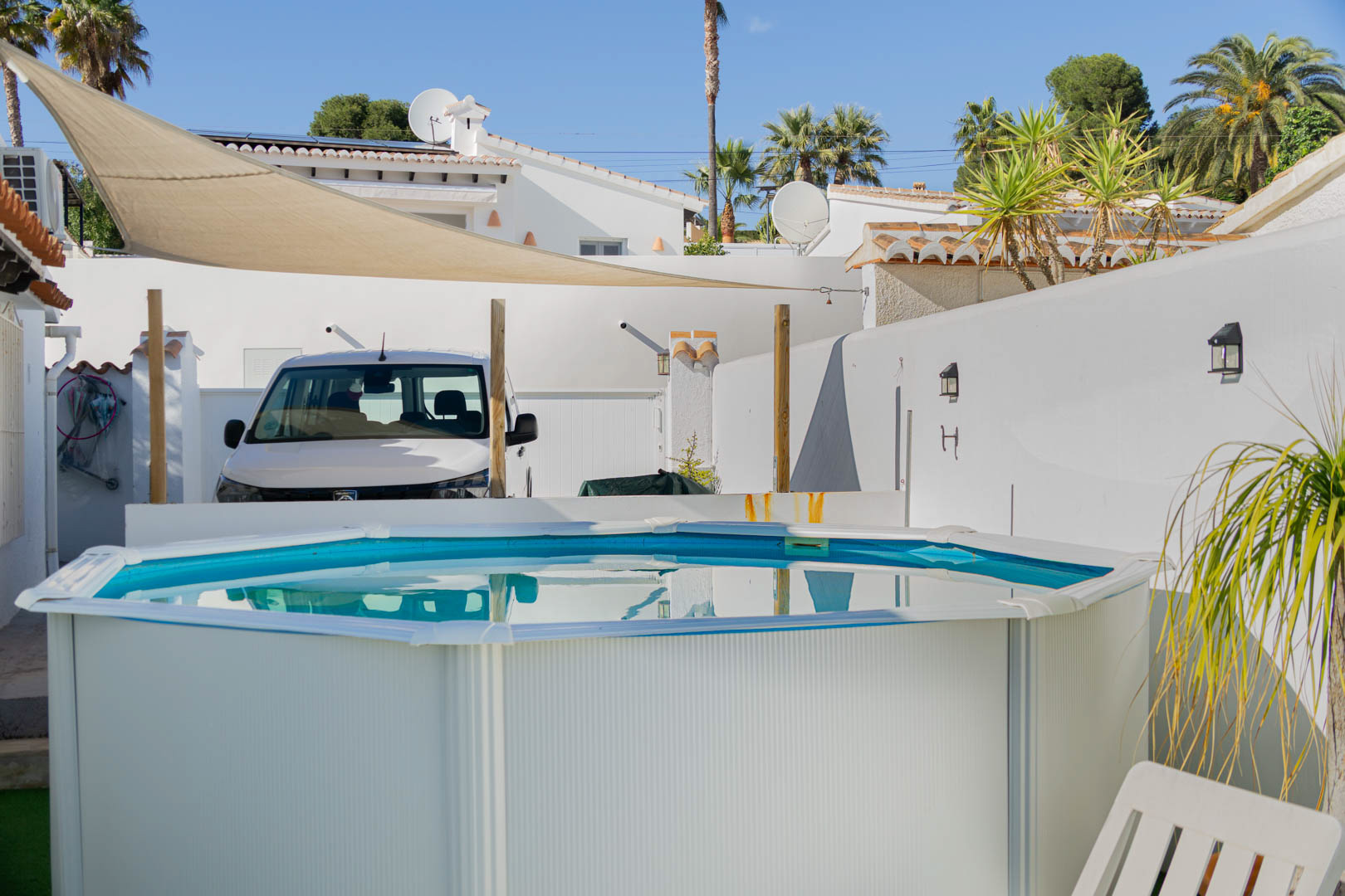 Achteckiger Aufstellpool auf einer sonnigen Terrasse mit beigefarbenem Sonnensegel, umgeben von weißen Mauern und Palmen.