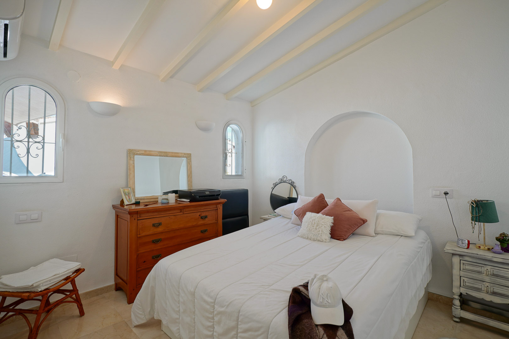Helles Schlafzimmer mit weiß gestrichenen Deckenbalken, Rundbogenfenstern und einer Wandnische. Ausgestattet mit Klimaanlage und Marmorboden.