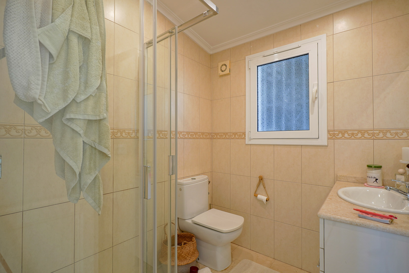 Komplettes Badezimmer mit cremefarbenen Fliesenwänden, Glasduschkabine, weißen Sanitäranlagen und einem Waschtisch mit Marmor-Arbeitsplatte.