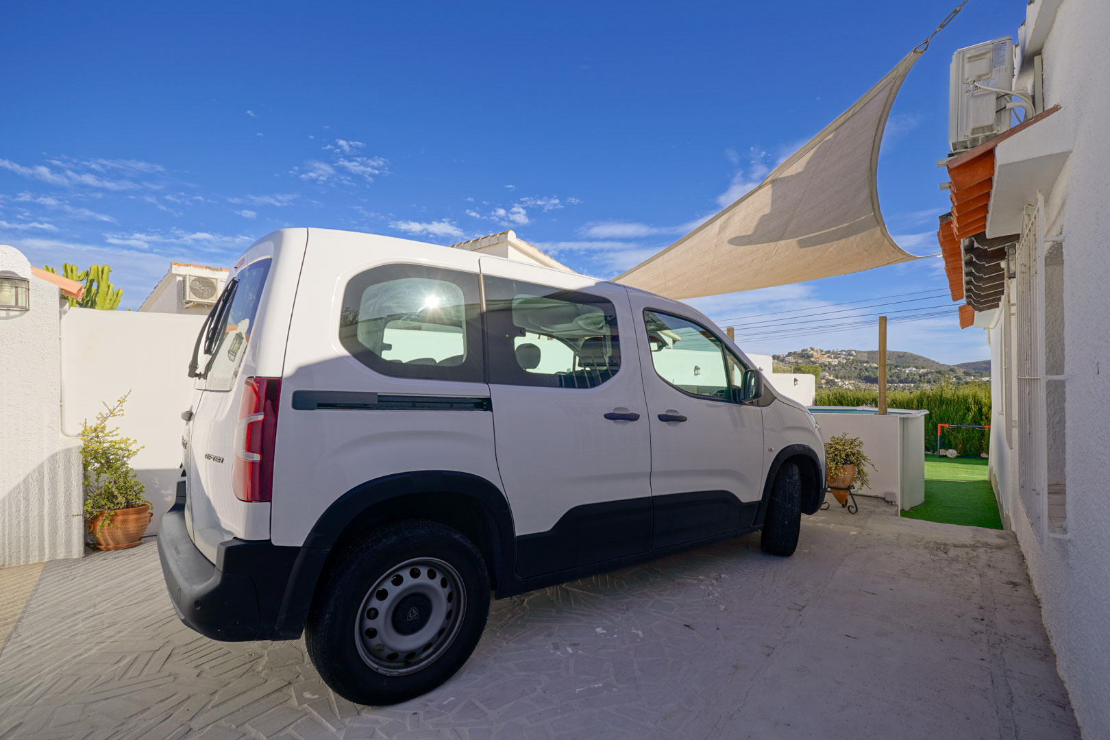 Privater Parkplatz mit gemustertem Pflaster und Sonnensegel, direkt an der weißen Fassade der Villa gelegen, mit Blick auf die umliegende Hügellandschaft.