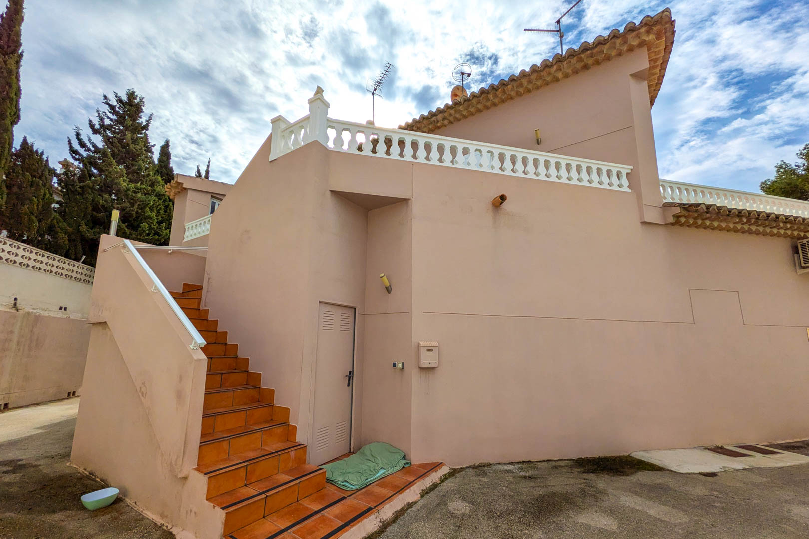 Außentreppe mit Terrakotta-Fliesen führt zum Obergeschoss, ergänzt durch eine lachsfarbene Fassade und eine Terrasse mit klassischer weißer Balustrade.