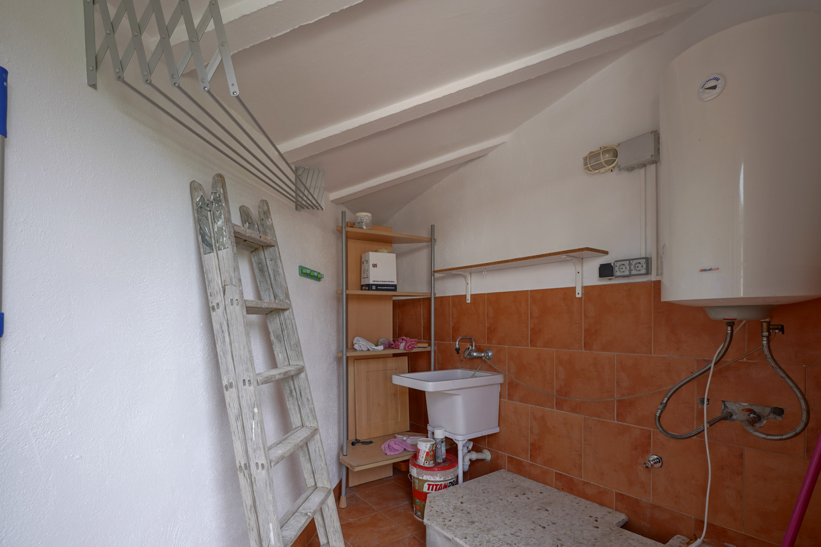 Funktionaler Hauswirtschaftsraum mit Dachschräge, Elektro-Warmwasserspeicher, Waschbecken und ausziehbarem Wandwäscheständer.