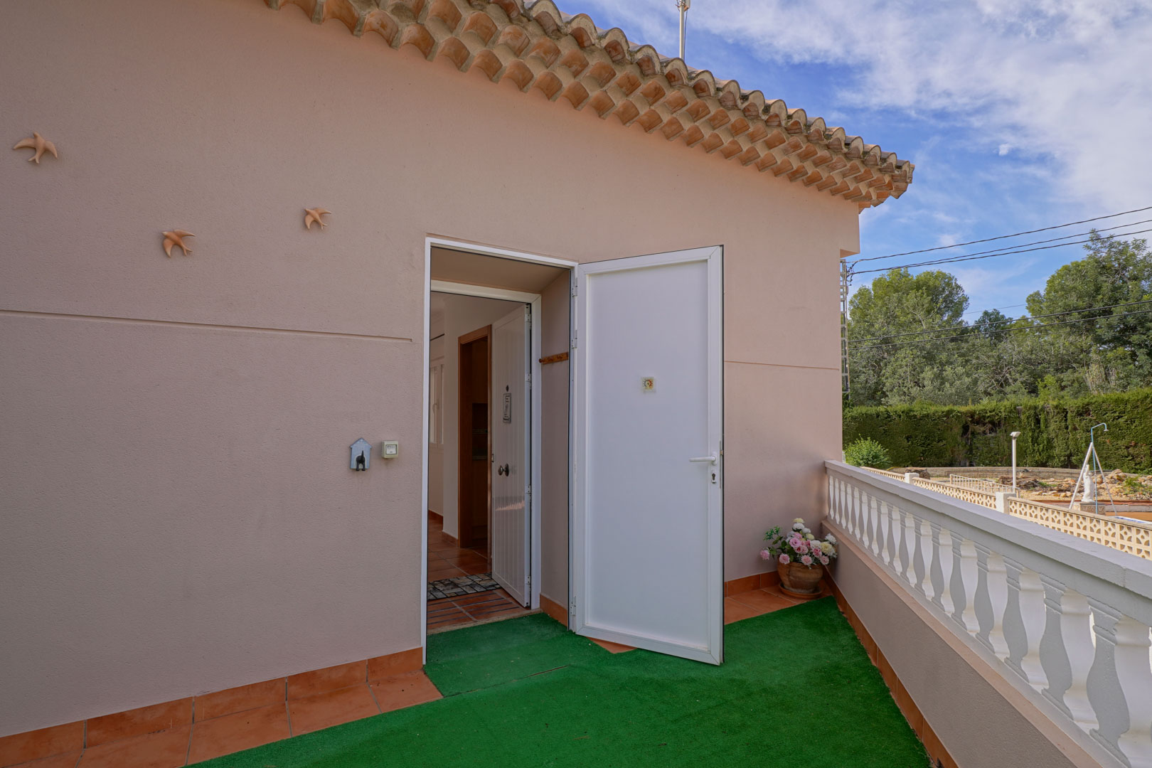 Haupteingang zum Penthouse von der oberen Terrasse aus, mit weißer Tür, Terrakottaboden und klassischer Balustrade mit Blick auf die Umgebung.