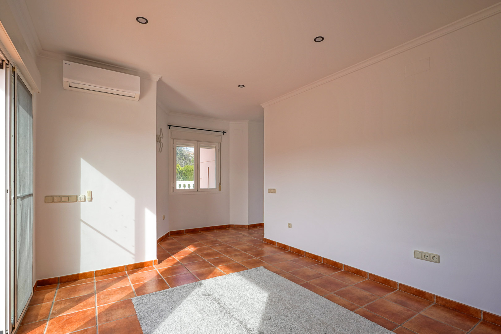 Heller Wohn-Essbereich mit rustikalen Terrakottafliesen, Split-Klimaanlage und direktem Zugang zur Außenterrasse durch Glastüren.