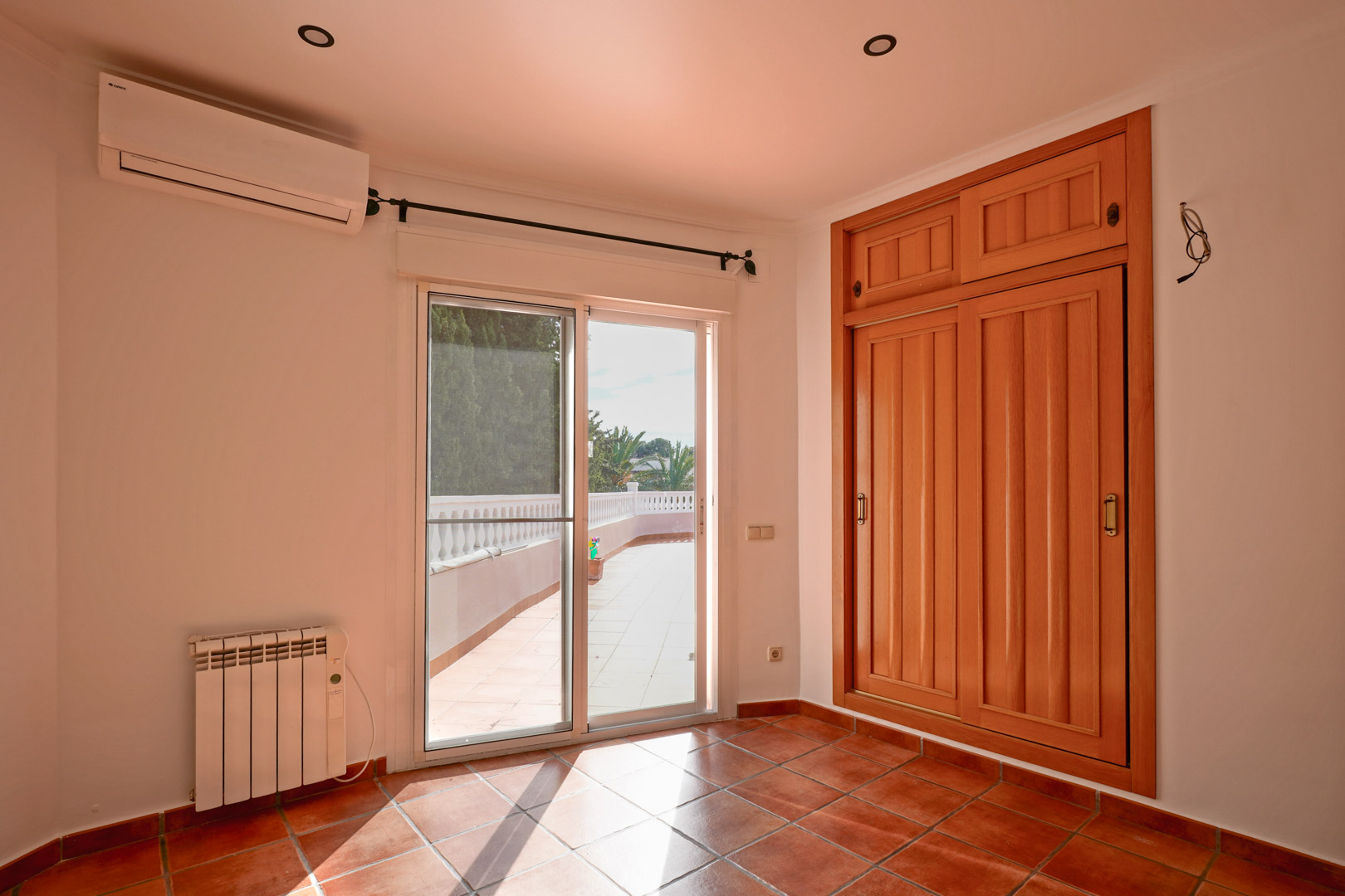 Schlafzimmer mit Einbauschrank aus Holz, Terrakottaboden und Terrassenzugang. Ausgestattet mit Klimaanlage, Elektroheizkörper und Deckeneinbaustrahler.