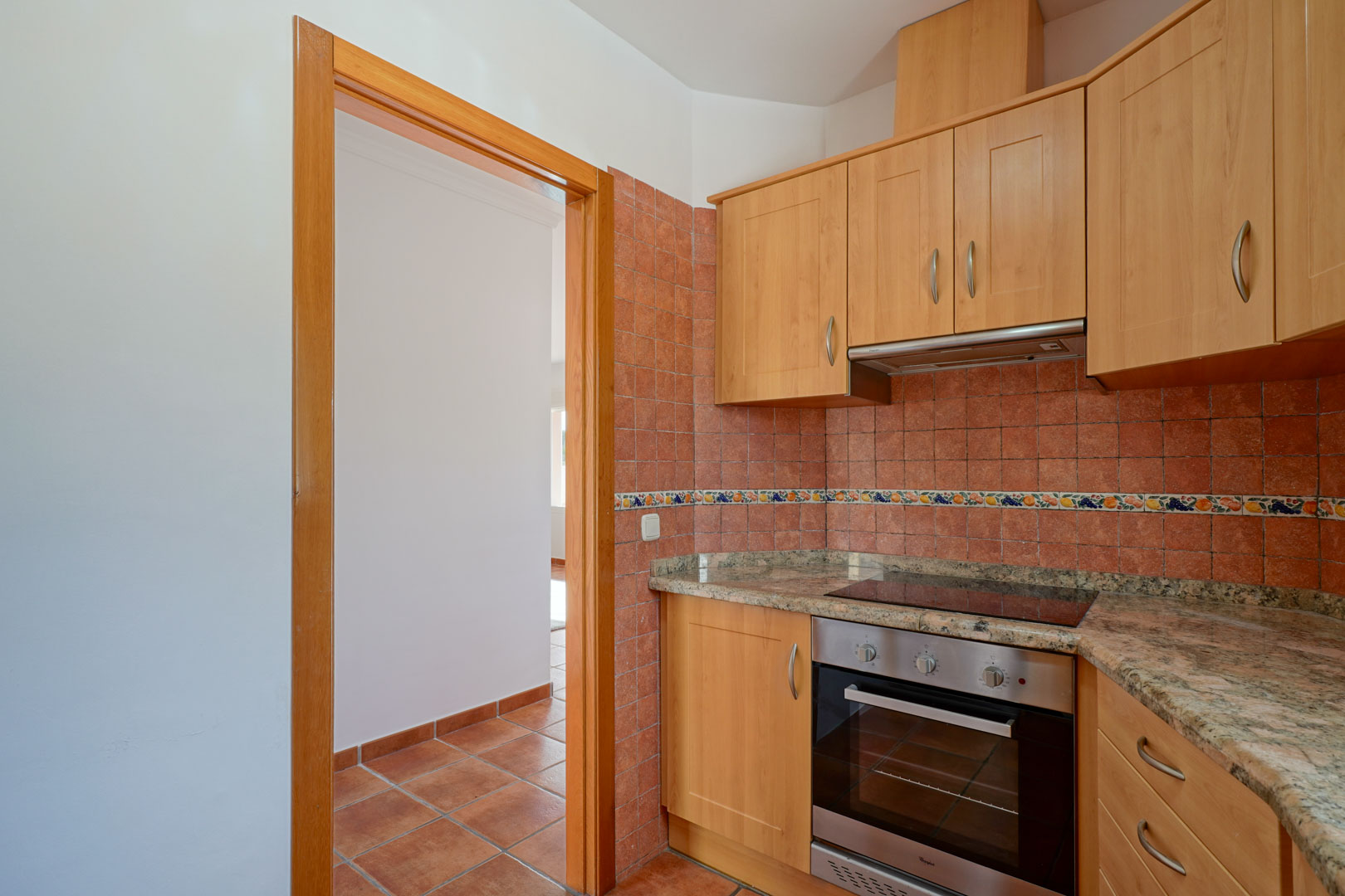 Separate Küche mit Holzschränken, Granitarbeitsplatte und integrierten Geräten. Rustikale Wandfliesen und ein Keramikboden in Terrakotta-Optik prägen den Raum.