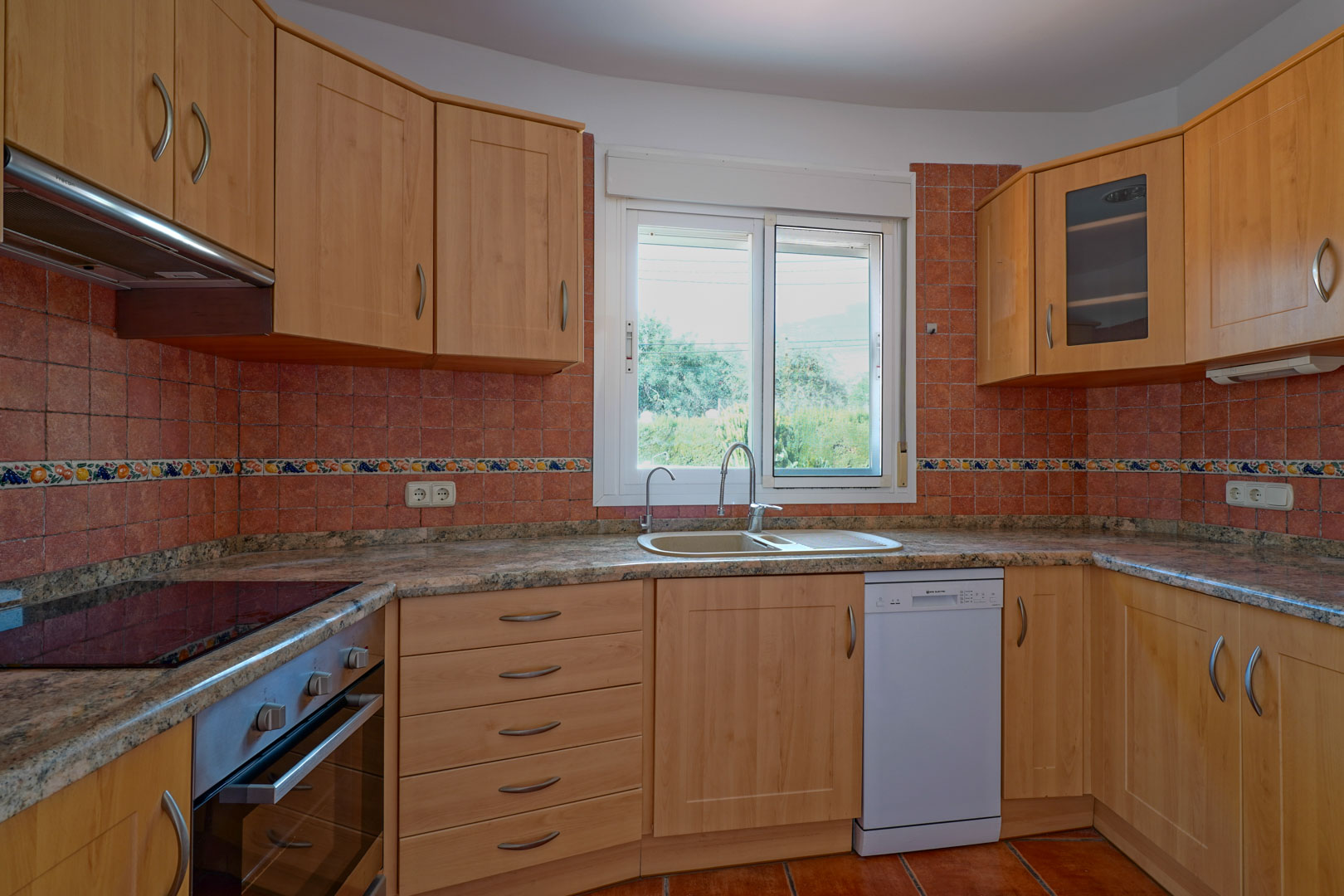 Separate Küche mit Holzschränken, Granitarbeitsplatte und rustikalem Fliesenspiegel. Ausgestattet mit Backofen, Geschirrspüler und einem Fenster mit Blick ins Grüne.